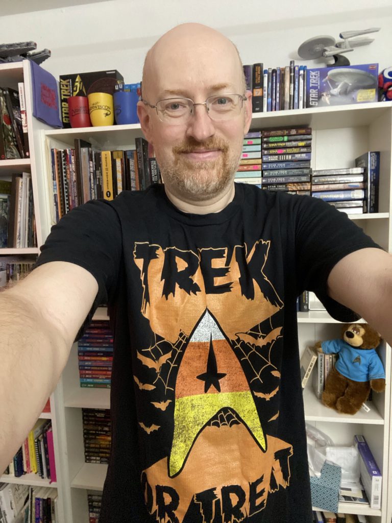 A photo of Michael Hanscom wearing a t-shirt with a Halloween styled version of the Star Trek logo and the text 'Trek or Treat'