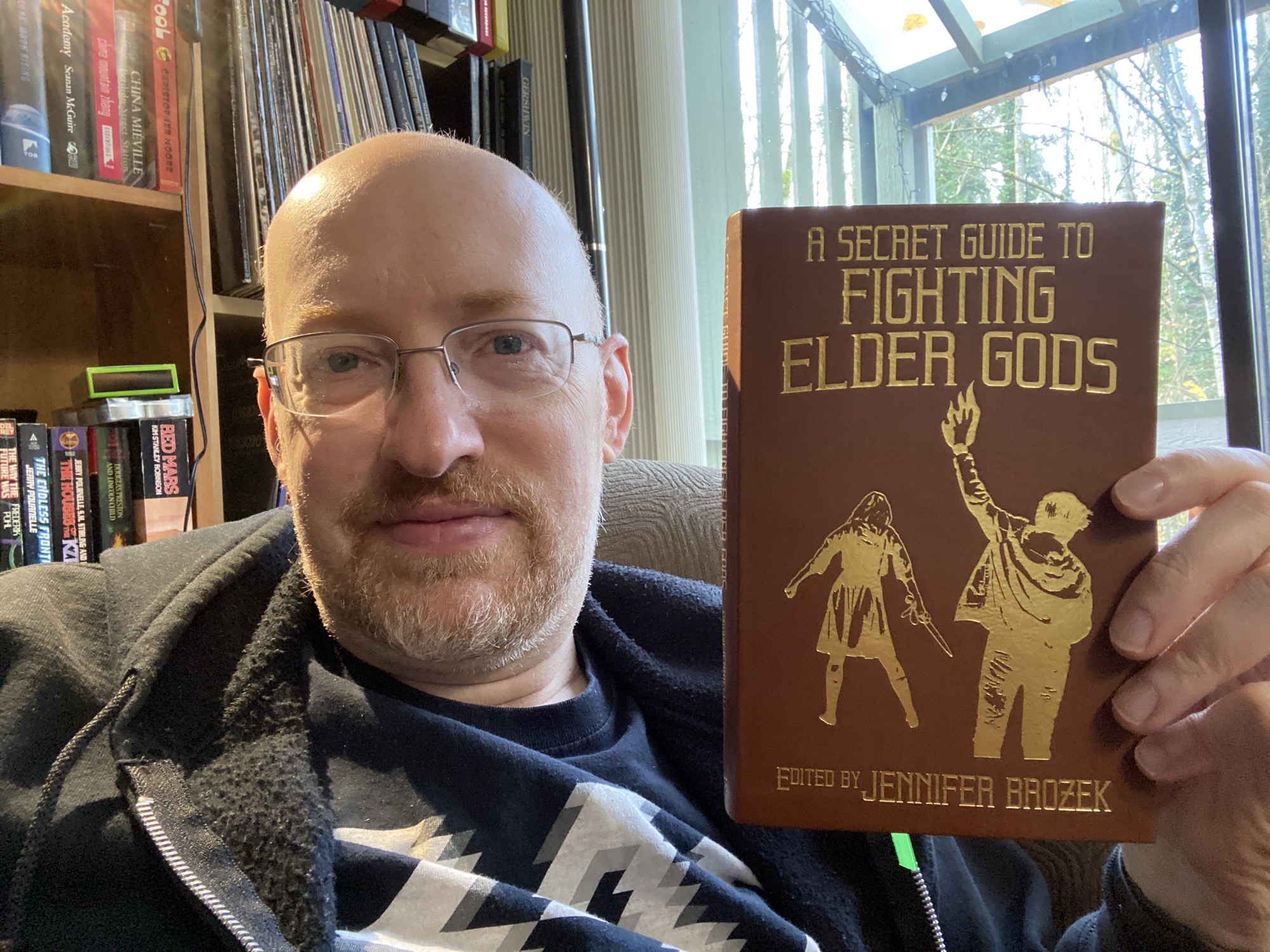 Photo of Michael Hanscom holding the book _A Secret Guide to Fighting Elder Gods_ edited by Jennifer Brozek