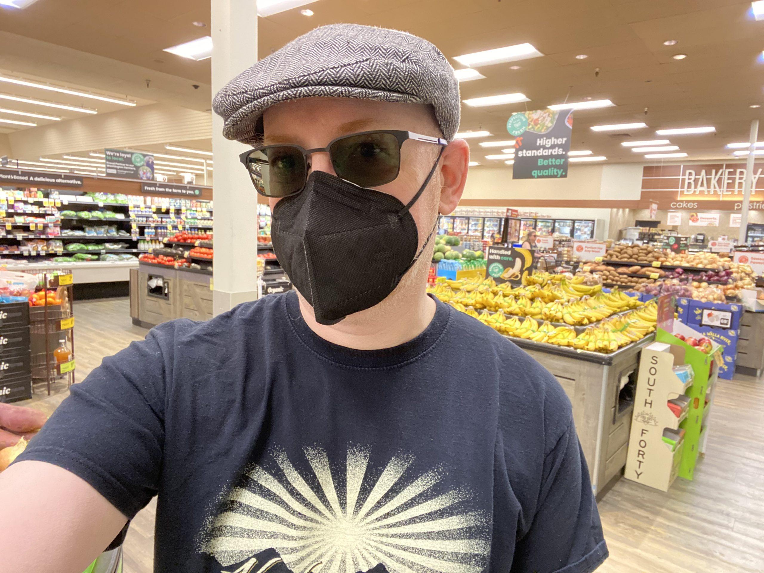 Me standing in a grocery store, wearing a grey cap, black t-shirt, black KN95 mask, and dark sunglasses.