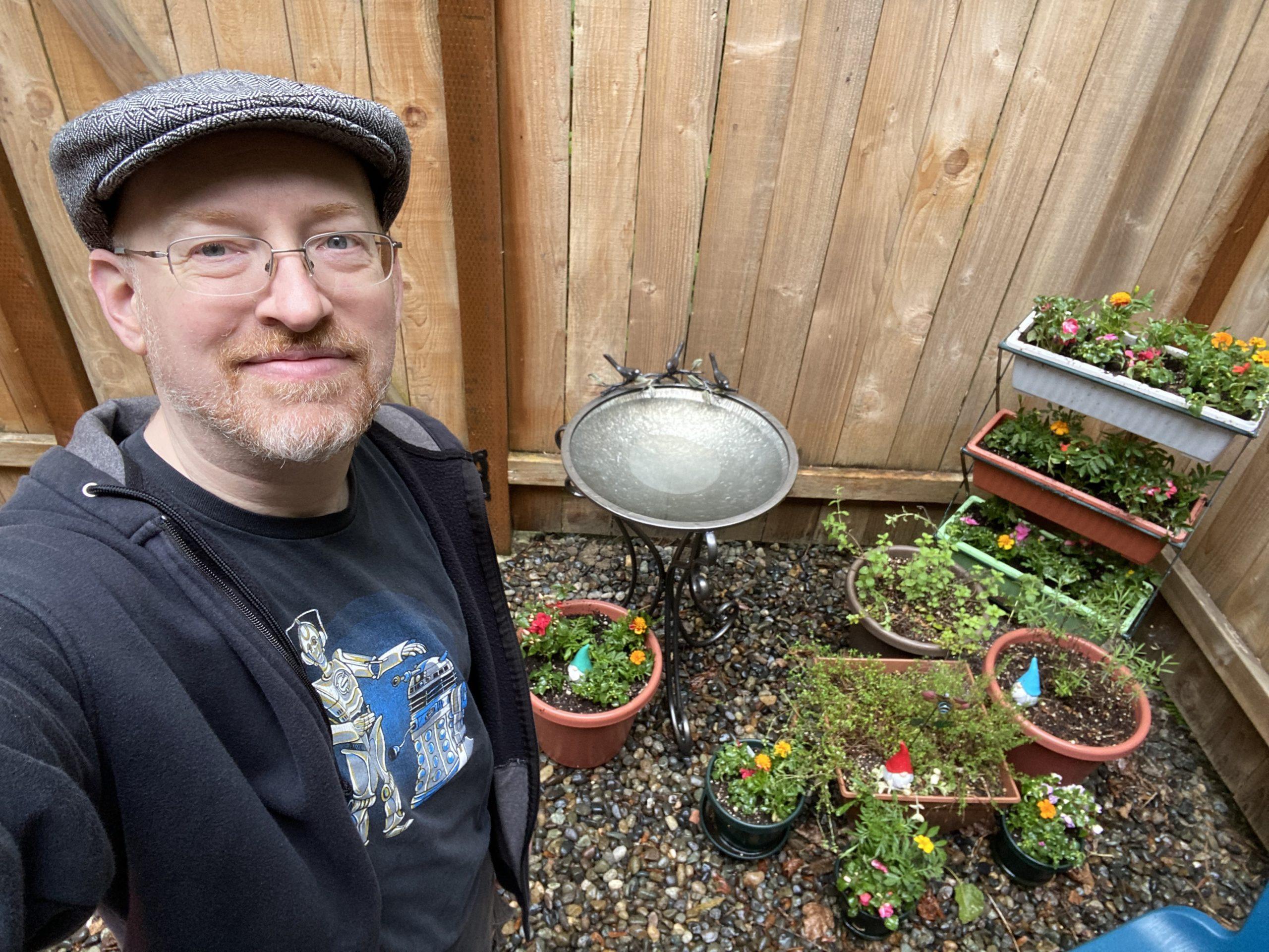 Me standing in front of a wooden fence, next to a metal birdbath and several freshly updated planters and flowerpots.