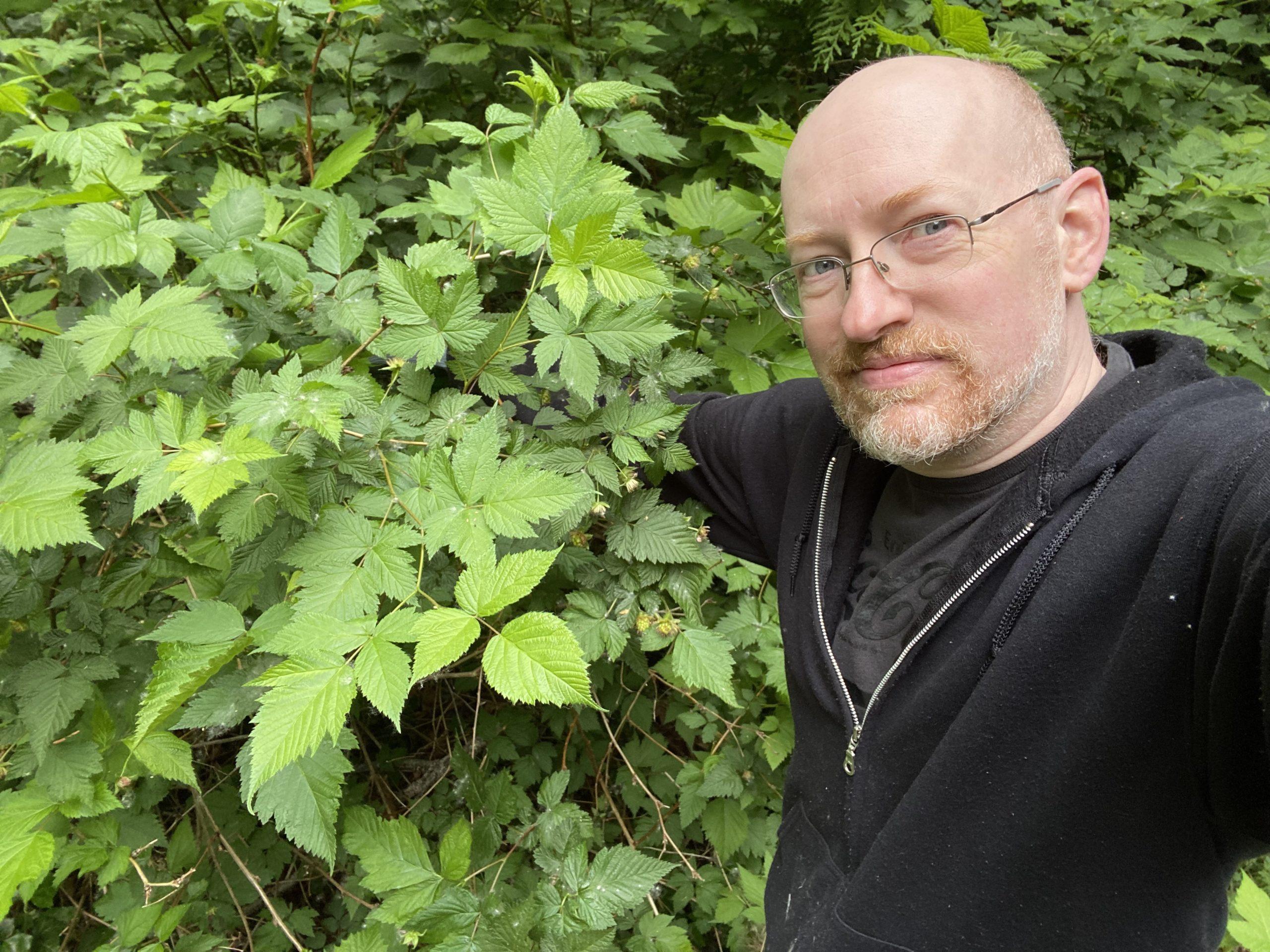 Me with a determined expression and one arm disappearing back into a bunch of green leaves.