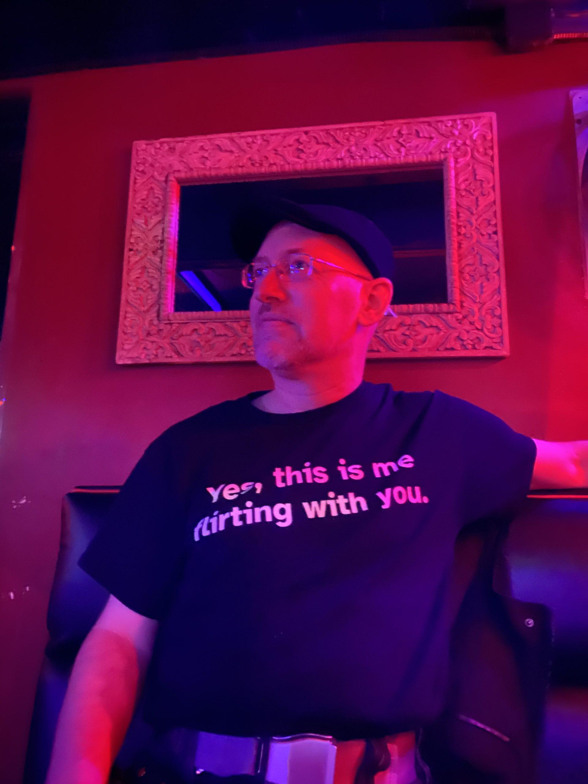 Me bathed in red light against a red wall, wearing my "Yes, this is me flirting with you" t-shirt.