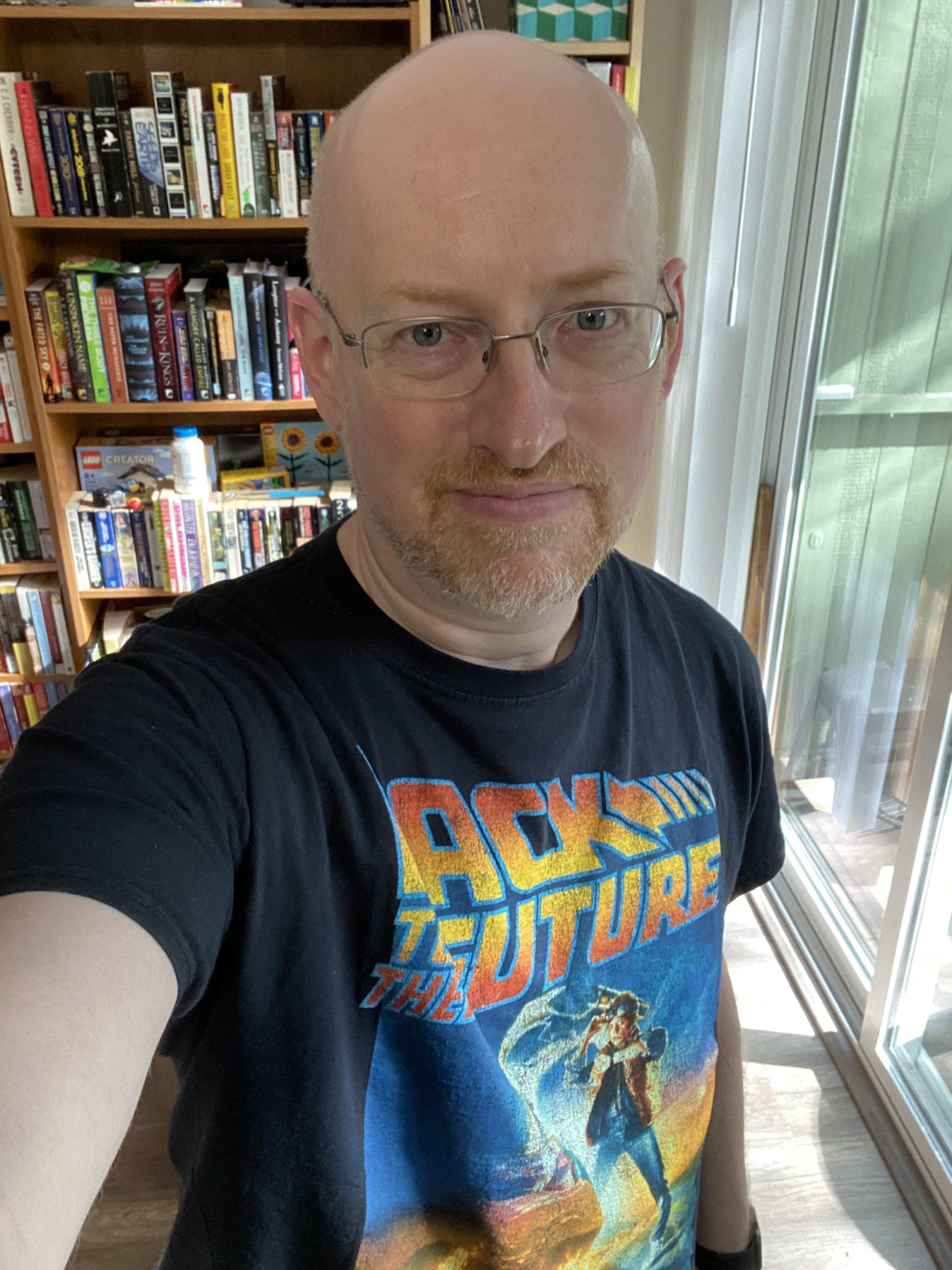 Me, slightly smiling, standing in front of a bookcase and wearing a black Back to the Future t-shirt.