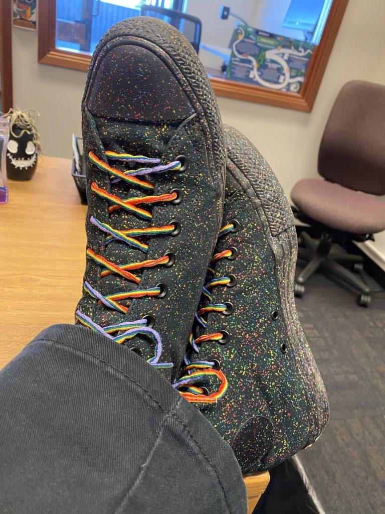 My feet crossed on the edge of my desk. I'm wearing Pride-themed Converse high-tops, black with rainbow speckles and with rainbow laces.