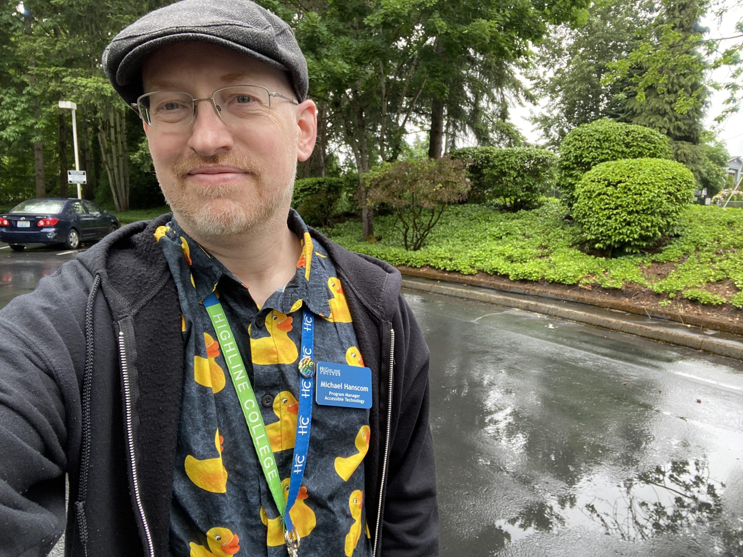 Me outside on a street freshly wet with rain, wearing a black hoodie over a black button-up shirt with a print of yellow rubber duckies.