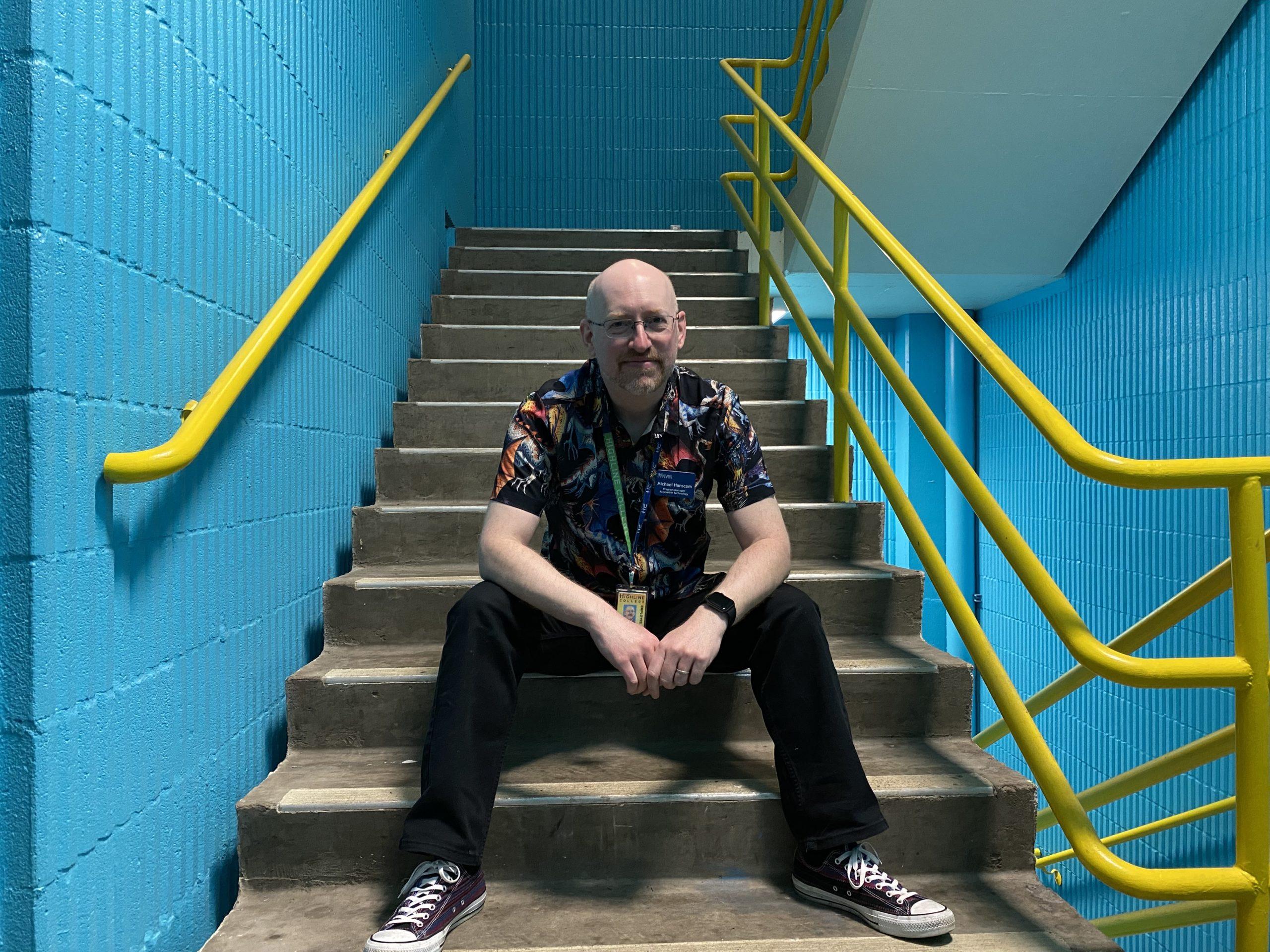 Me sitting in an industrial-looking stairwell with blue walls and metal railings. I have a somewhat bemused expression on my face.