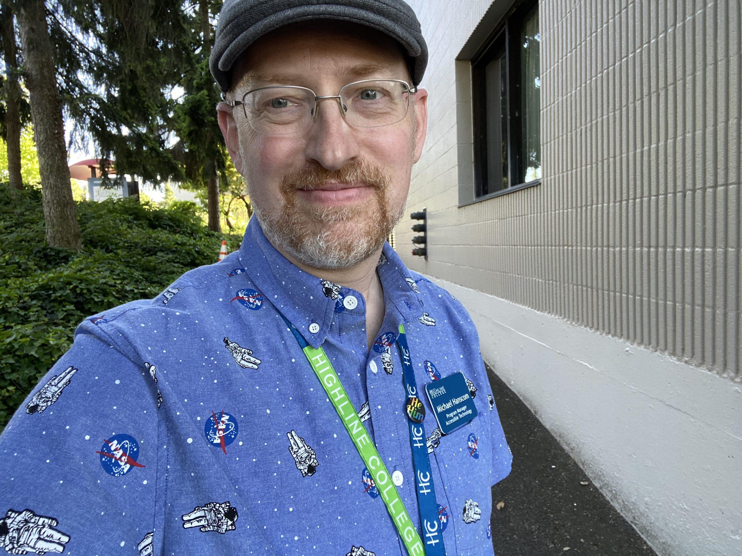 Me standing outside one of the buildings on campus, wearing a blue button-up short-sleeve shirt with a print of stars, astronauts, and the NASA logo.