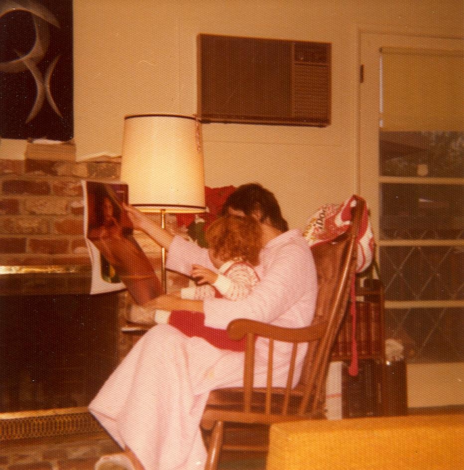 An old photo of me at around three years old, sitting in my mom’s lap as she sits in a rocking chair, dressed in a pink robe, holding up a Playboy centerfold and showing it to me.