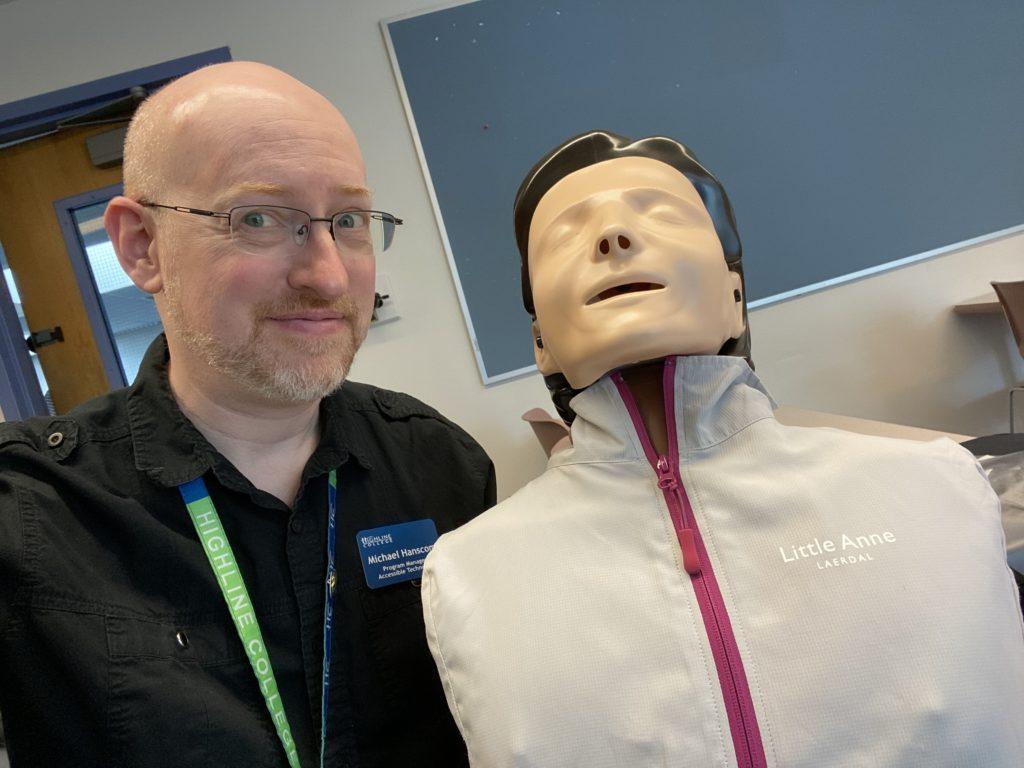 Me in a classroom with an amused look on my face holding a CPR practice dummy.