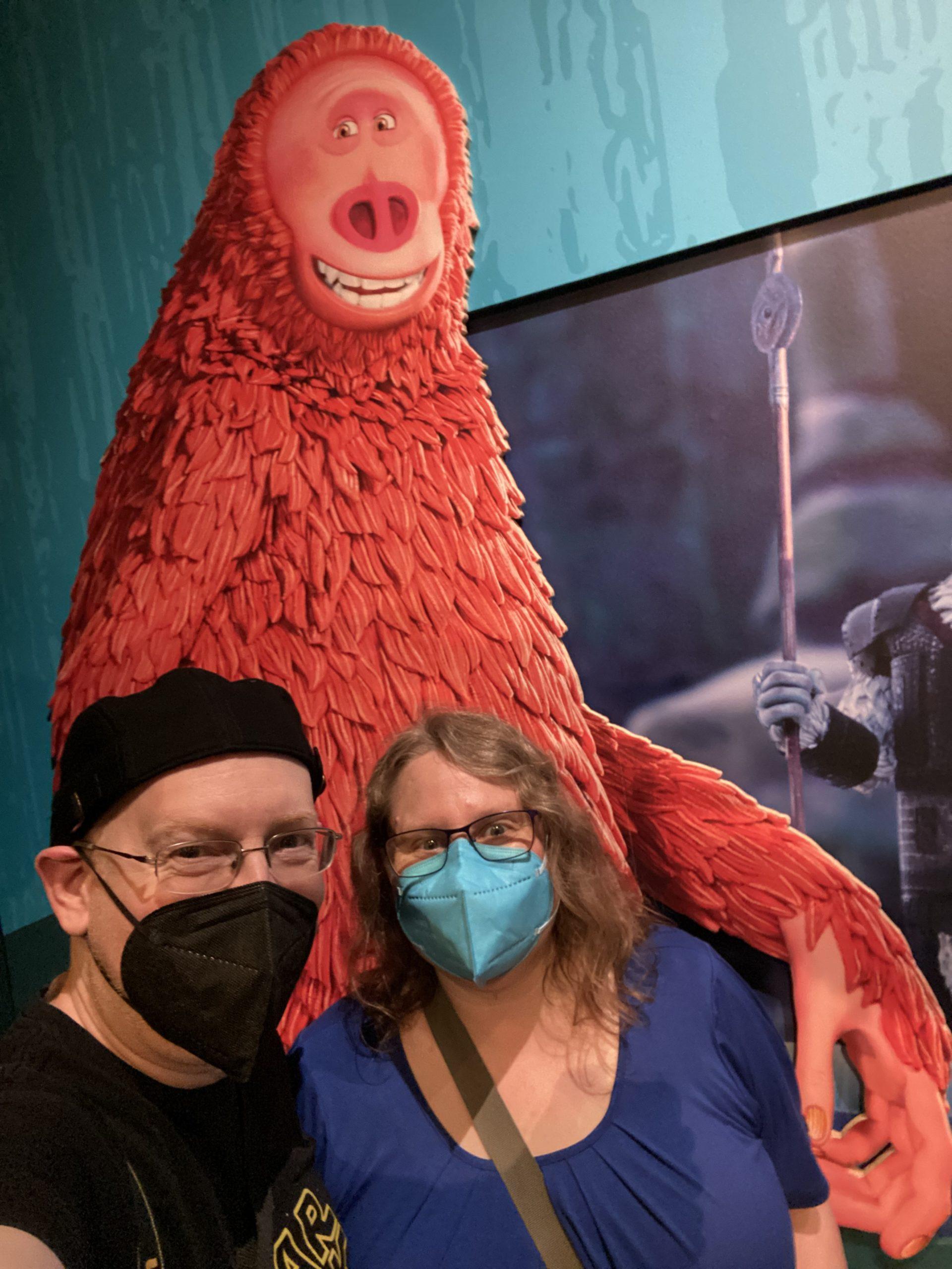 My wife and I in front of an image of the Bigfoot Mr. Link character from the Laika film Missing Link. We are standing so that it looks like Mr. Link has his arm around my wife's shoulders.