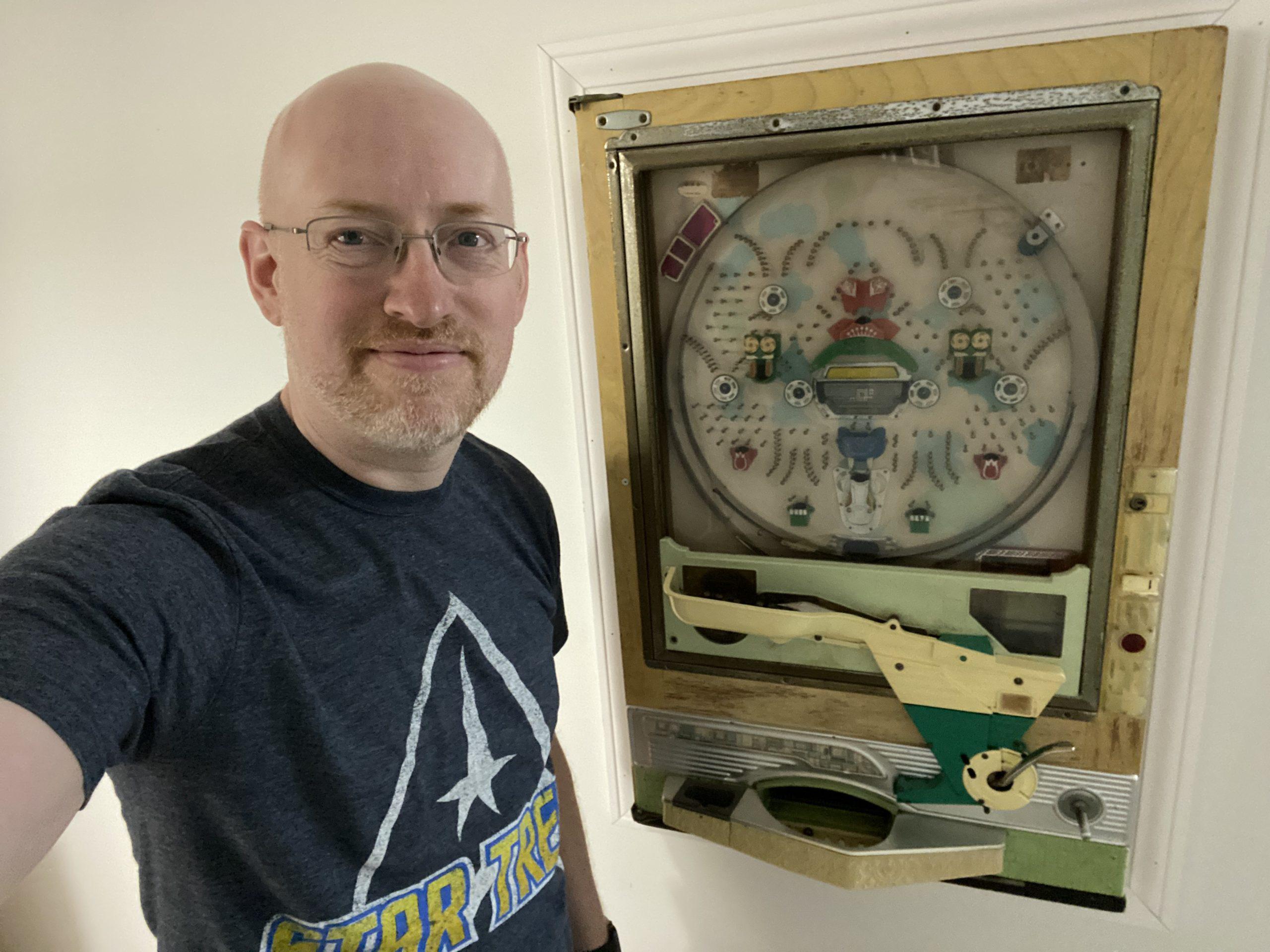 Me standing next to a vintage pachinko machine set into a wall.