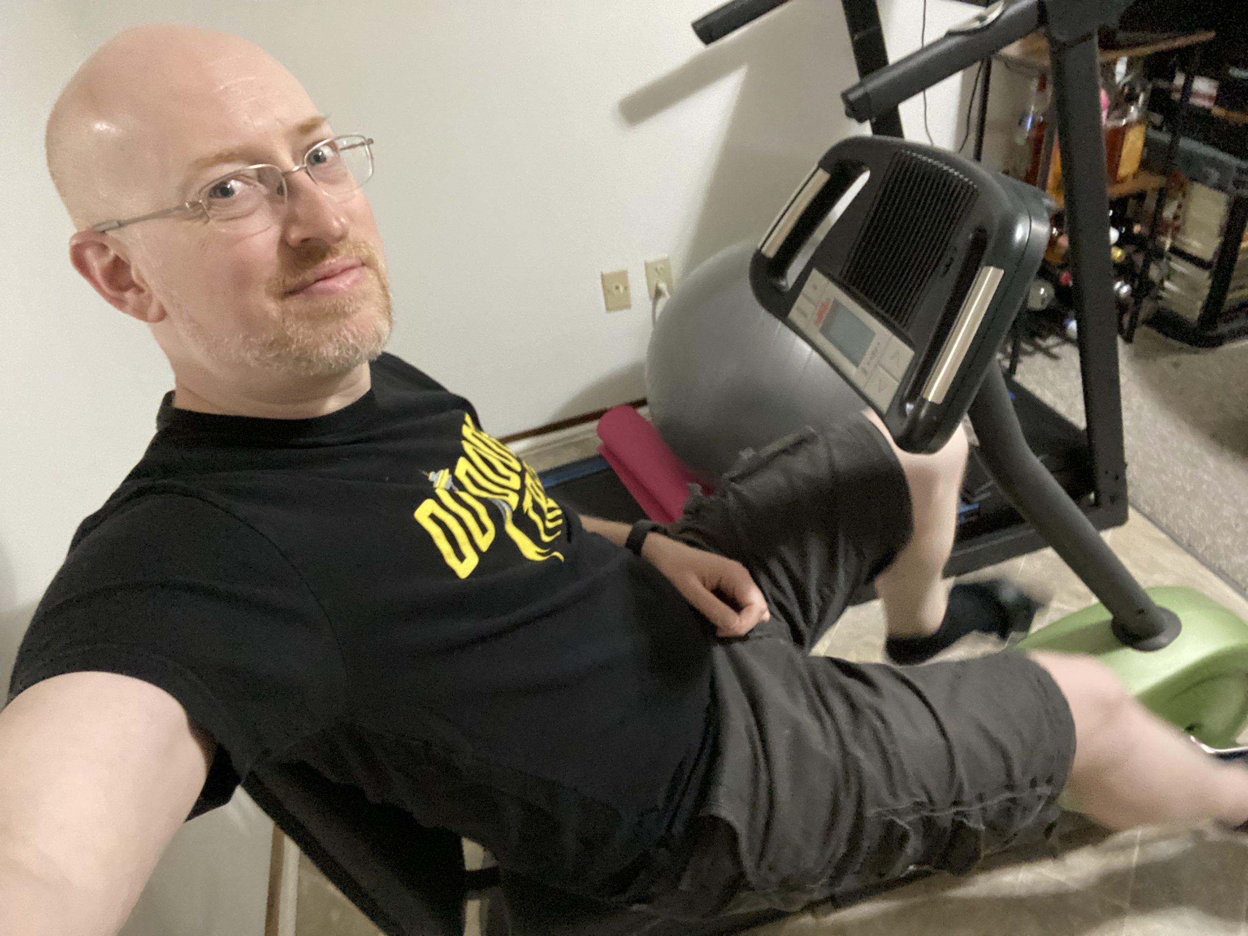 Me pedaling on a recumbant exercise bike; a treadmill is visible behind me.