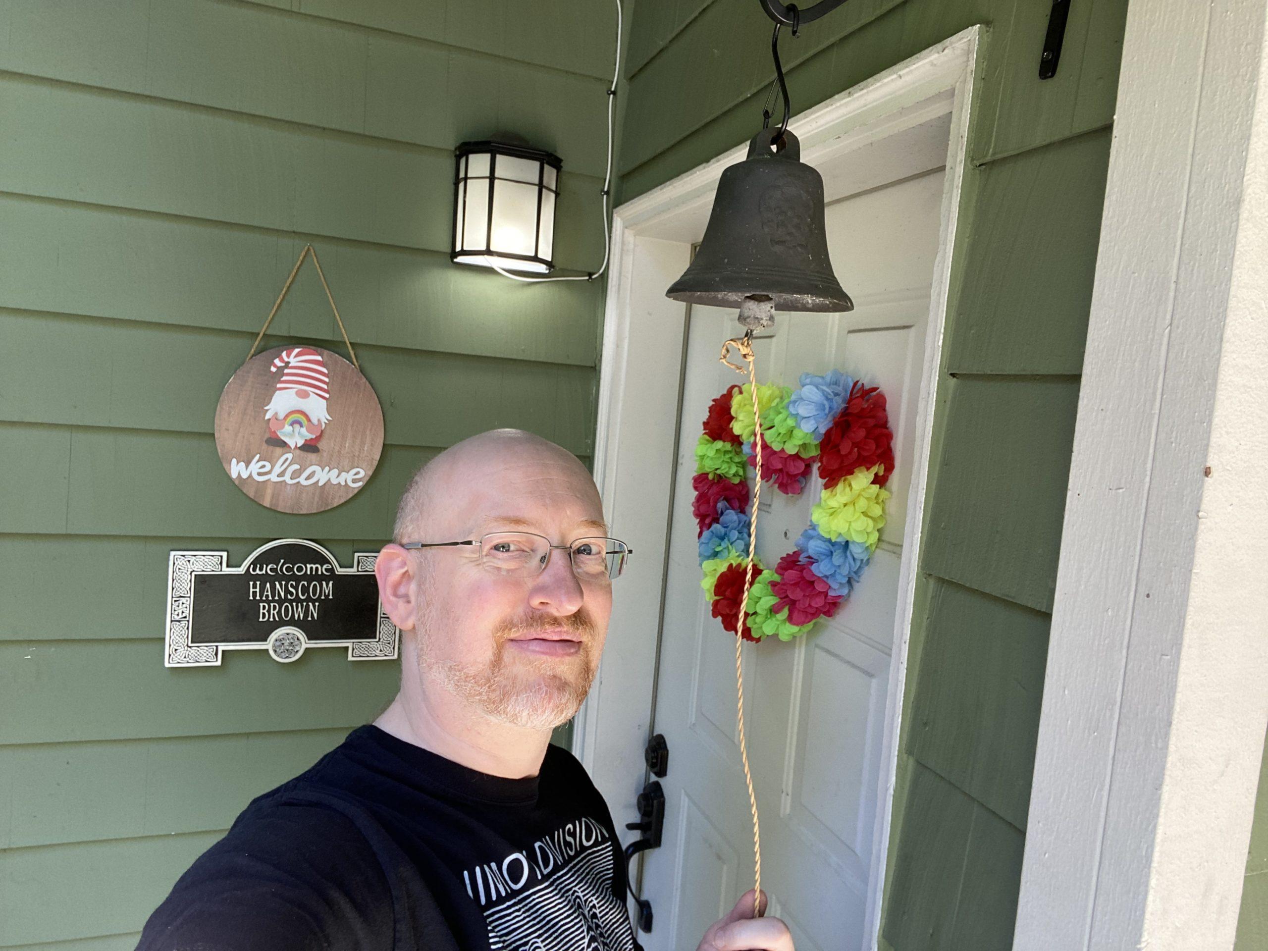 Me standing outside our front door, holding onto the pull rope dangling from an antique cast-iron bell hanging next to our door.