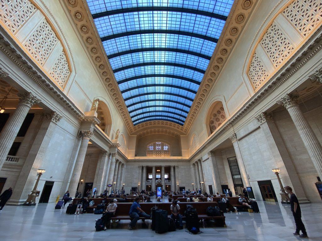 The main lobby of Chicago’s Union Station. It has a polished grey marble floor, white marble walls, ornate columns, and a high ceiling with gold ornamentation and a large arched glass roof.