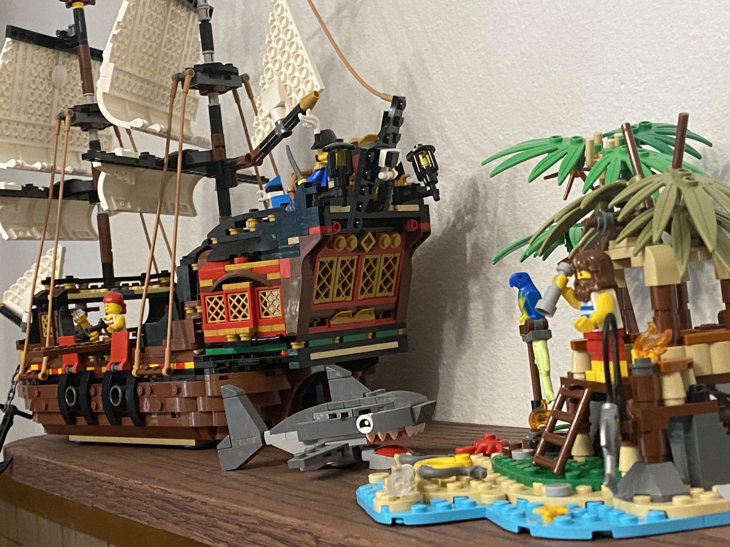 A Lego pirate ship, shark, and castaway on an island, viewed from behind the ship with the island in the foreground.