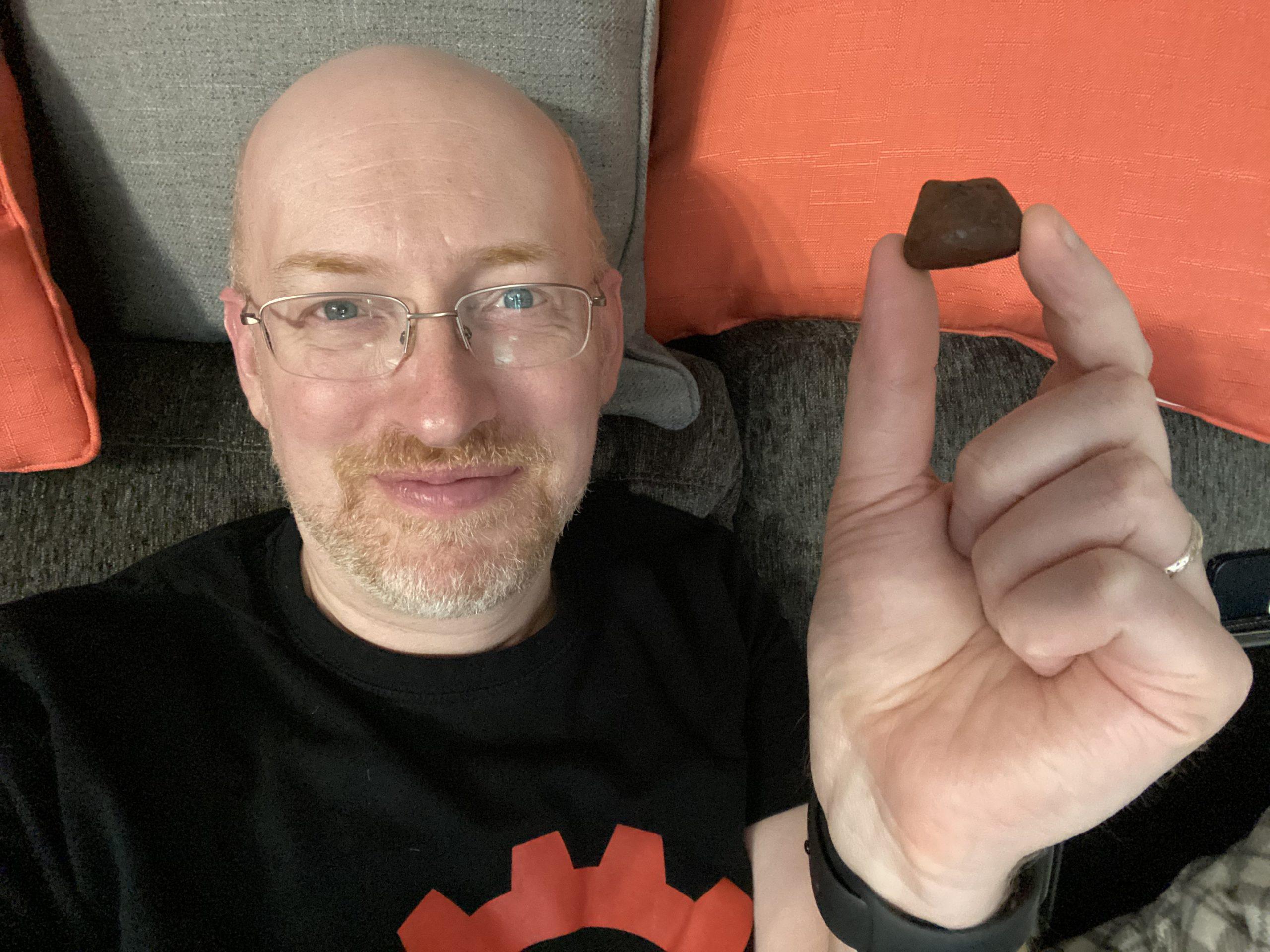 Me flopped on our couch against grey and orange pillows, smiling and holding up a small chocolate truffle.