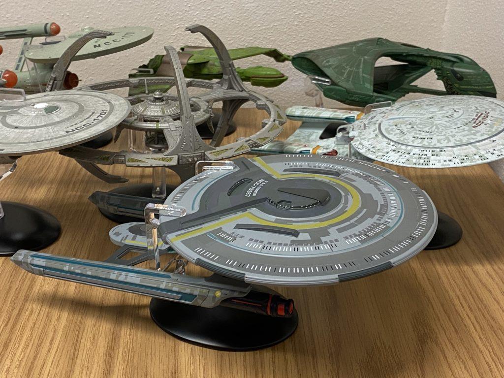 Another view of the collection of Star Trek ship models on my work desk. Visible is the original TOS USS Enterprise, the TOS Klingon Bird of Prey, the TNG Romulan Warbird, the TNG 1701-D Enterprise, Deep Space Nine, the Strange New Worlds USS Enterprise, and the Lower Decks USS Cerritos.