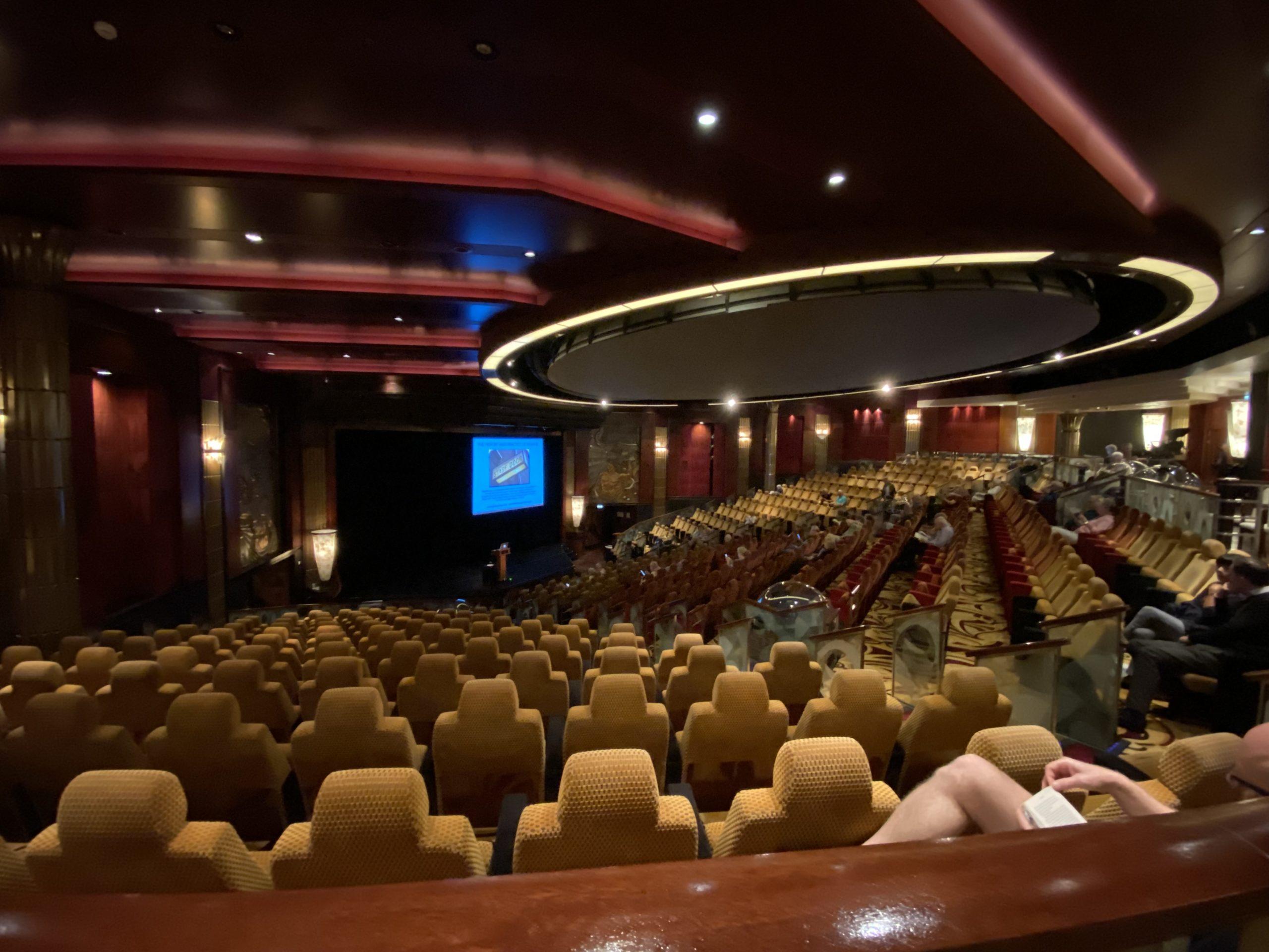 A large auditorium in reds golds, and beiges, with a dome screen set into the ceiling.