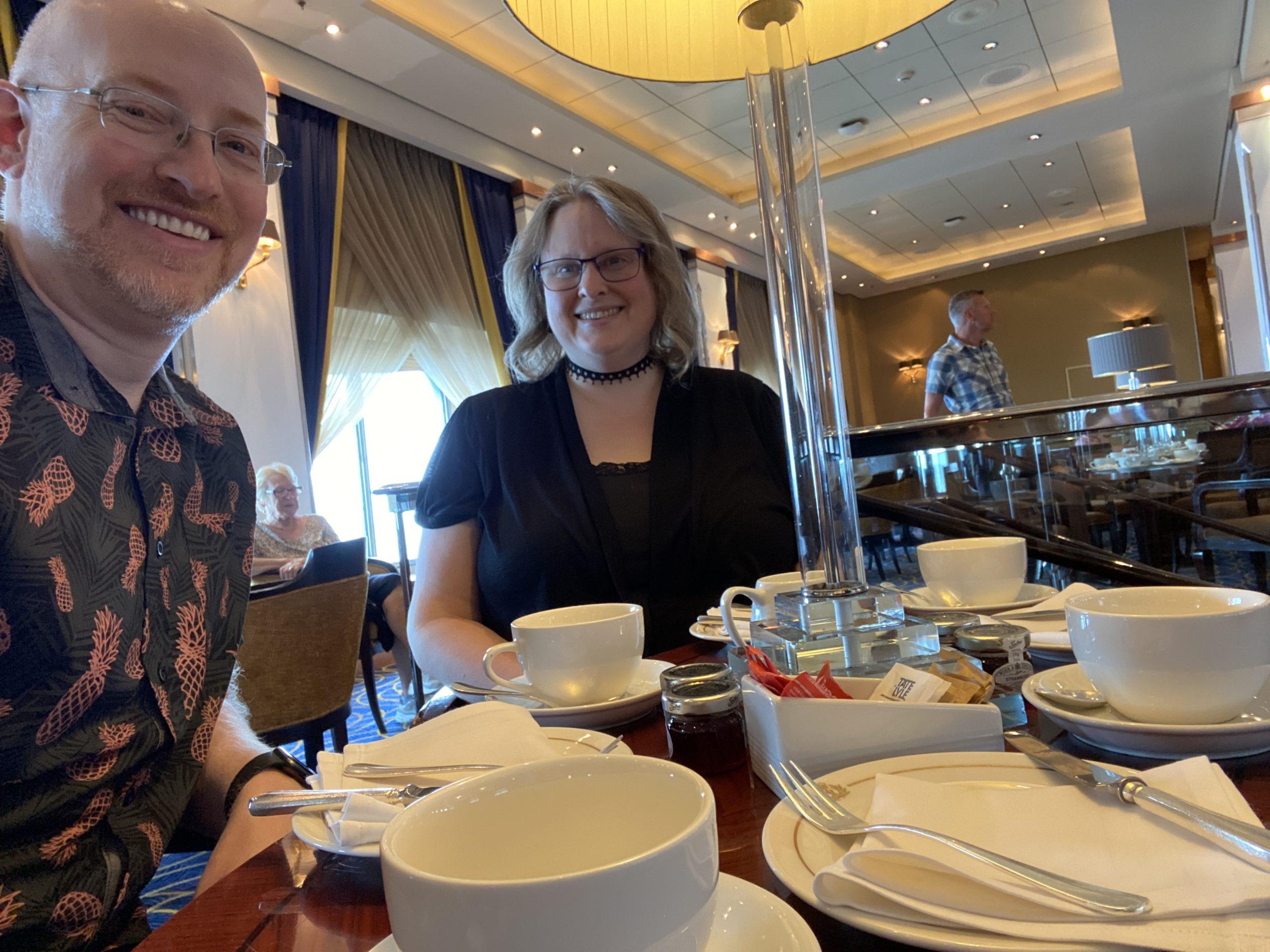 My wife and I sitting at a table all set up for a fancy traditional English tea service.