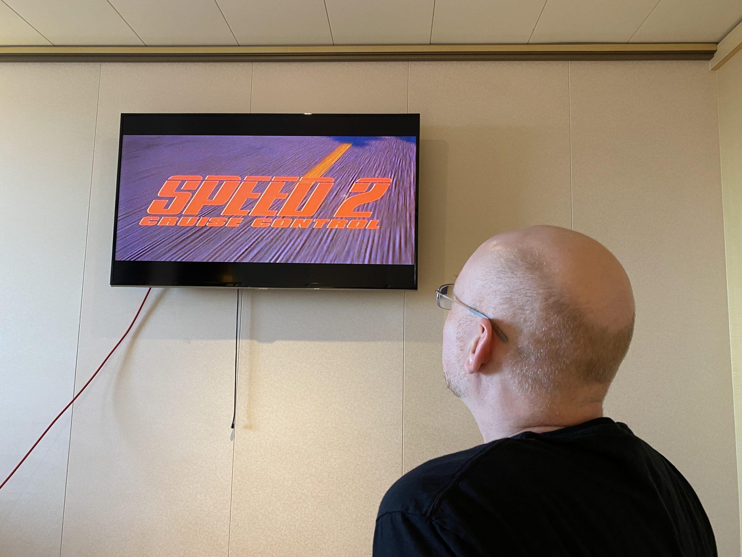 Me seen from behind, looking at the TV in our stateroom, showing the title card for the film Speed 2: Cruise Control.