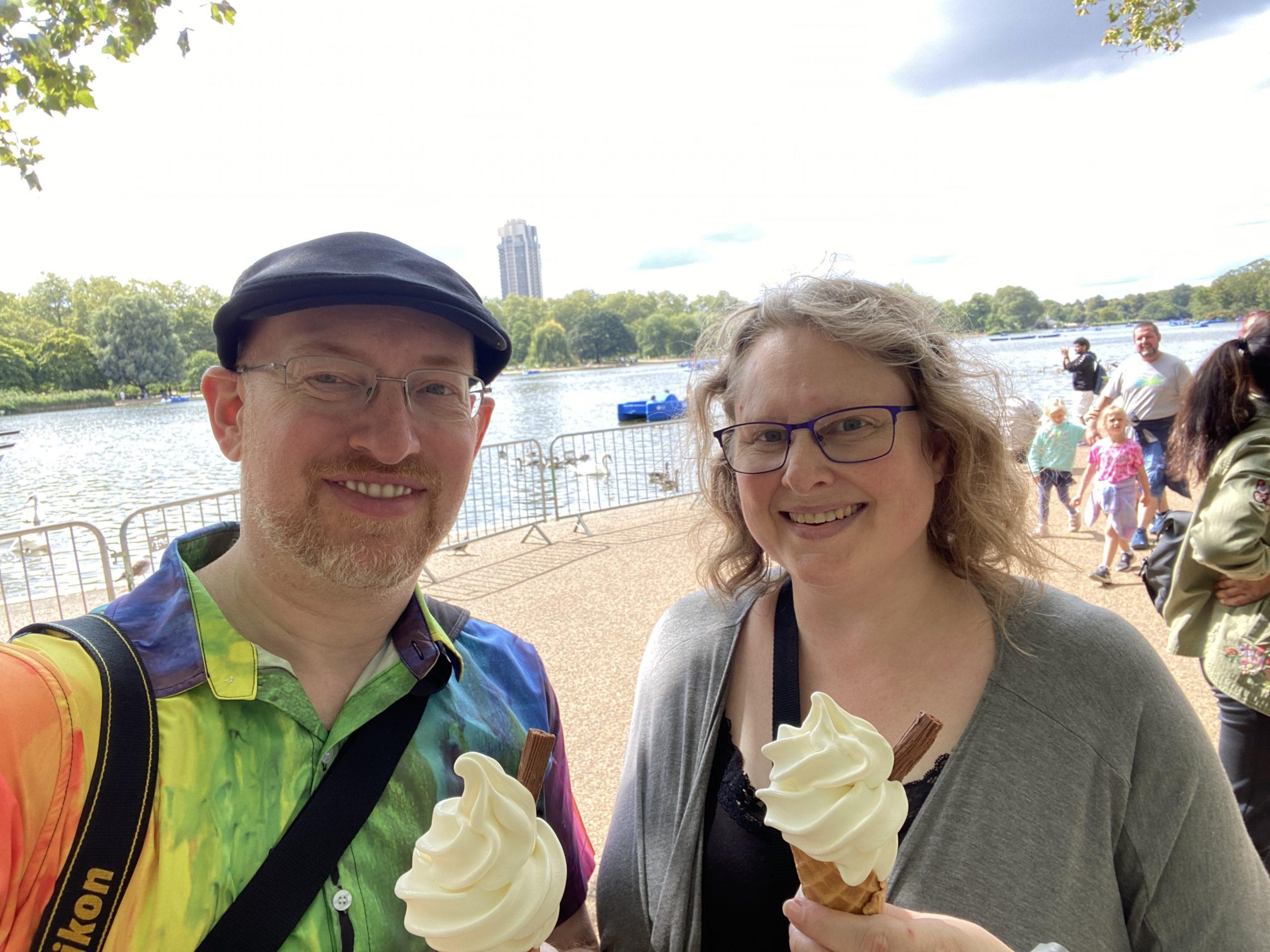 My wife and I holding soft-serve ice cream cones with flakey chocolate sticks in them in front of the lake at Hyde Park.