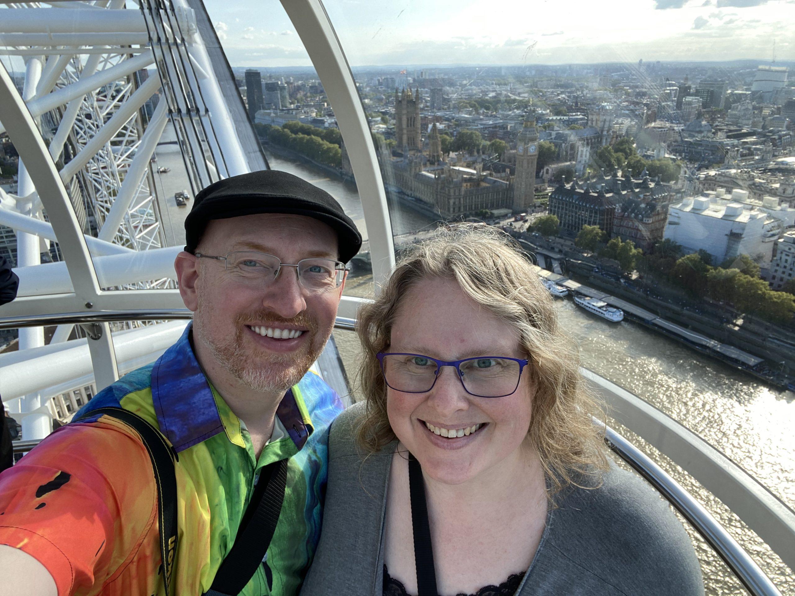 My wife and I in one of the carriages of the London Eye ferris wheel; the Palace of Westminster, Big Ben, Westminster Abbey, and the Thames are visible behind and below us.