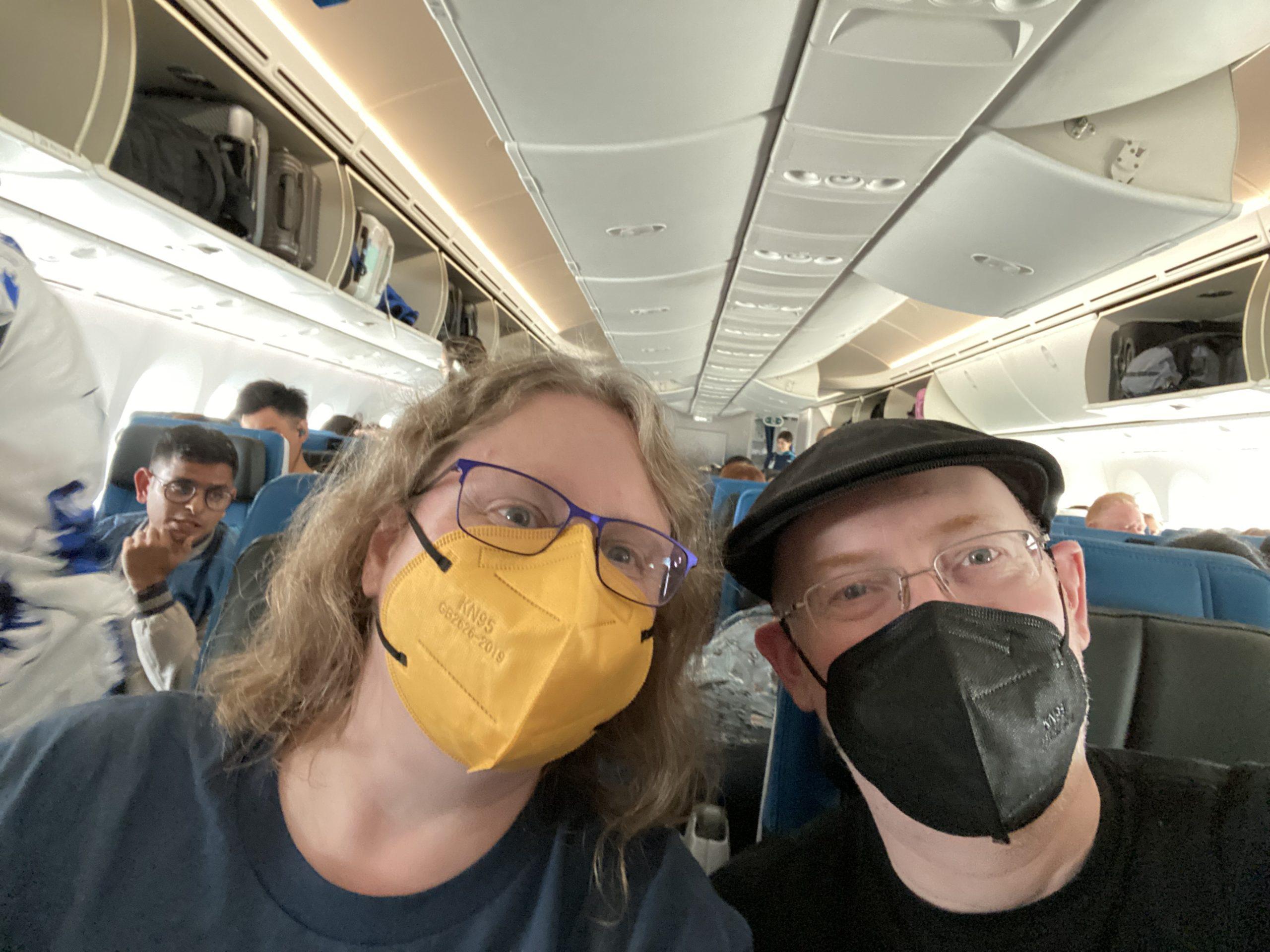 My wife and I, masked, seated in an airplane.