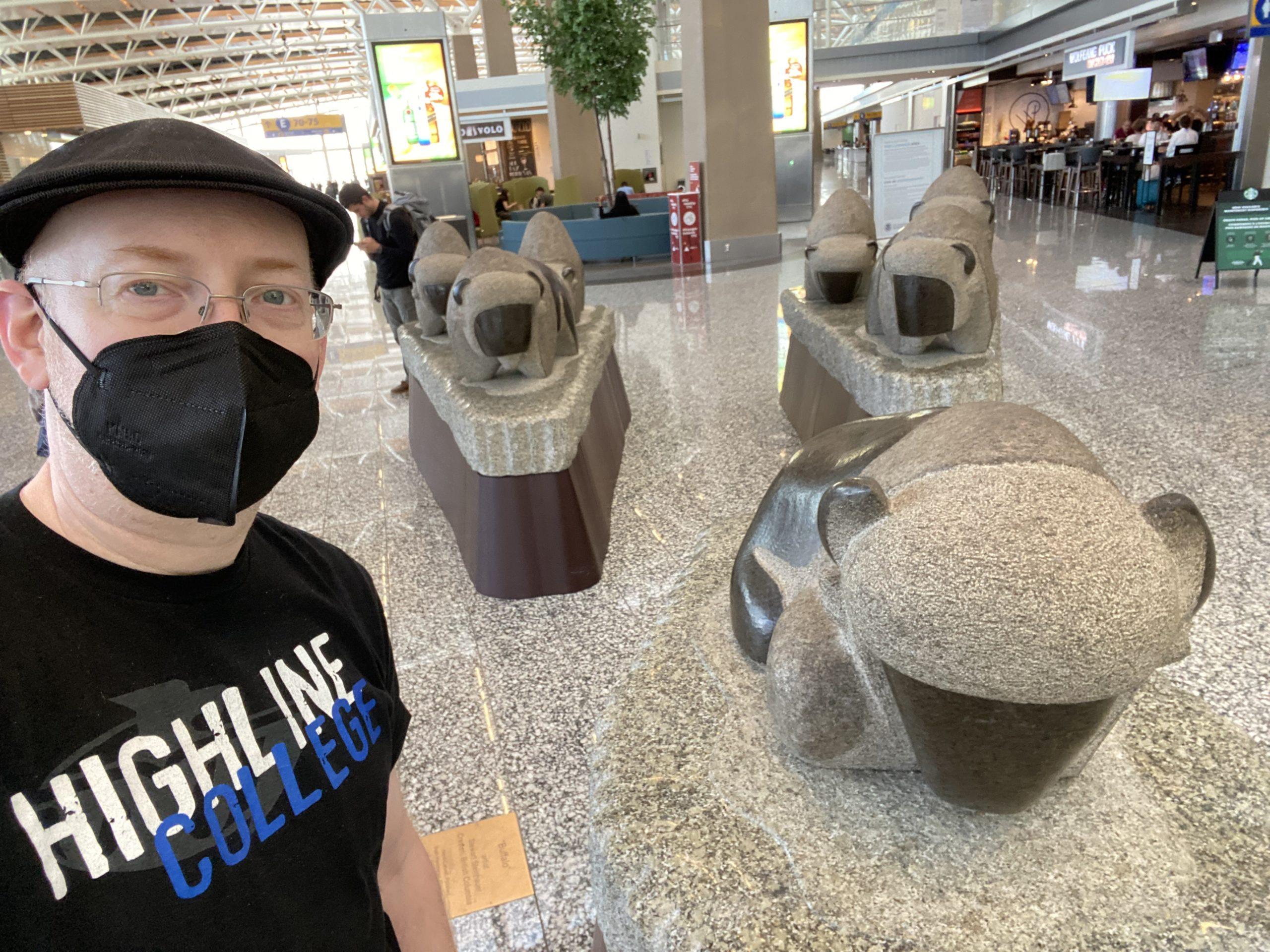 Me standing in front of an airport sculpture of bison, done in a very rounded and cute style.