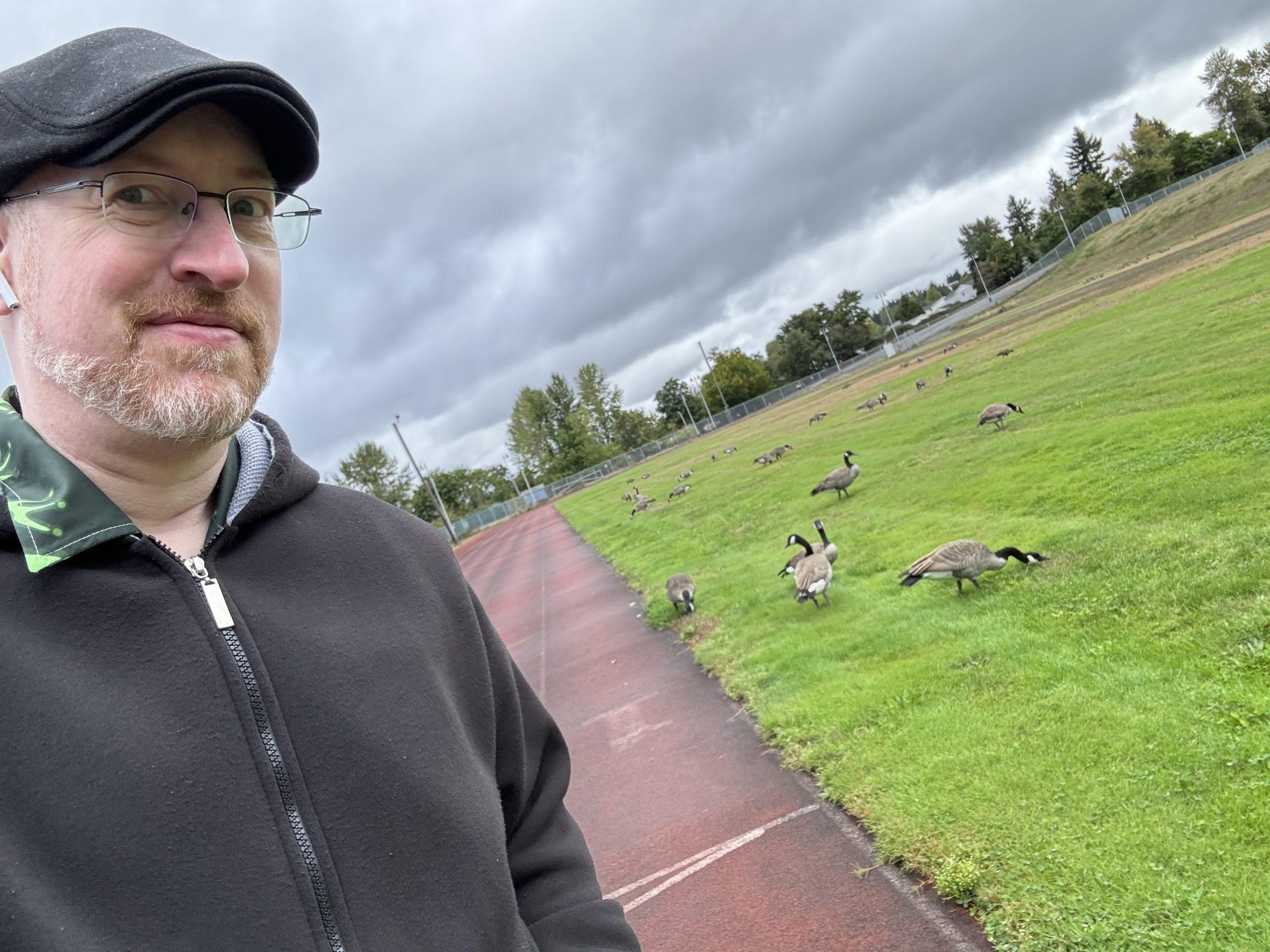 Me on a running track, with a flock of Canadian geese snacking in the grass in the center of the track.