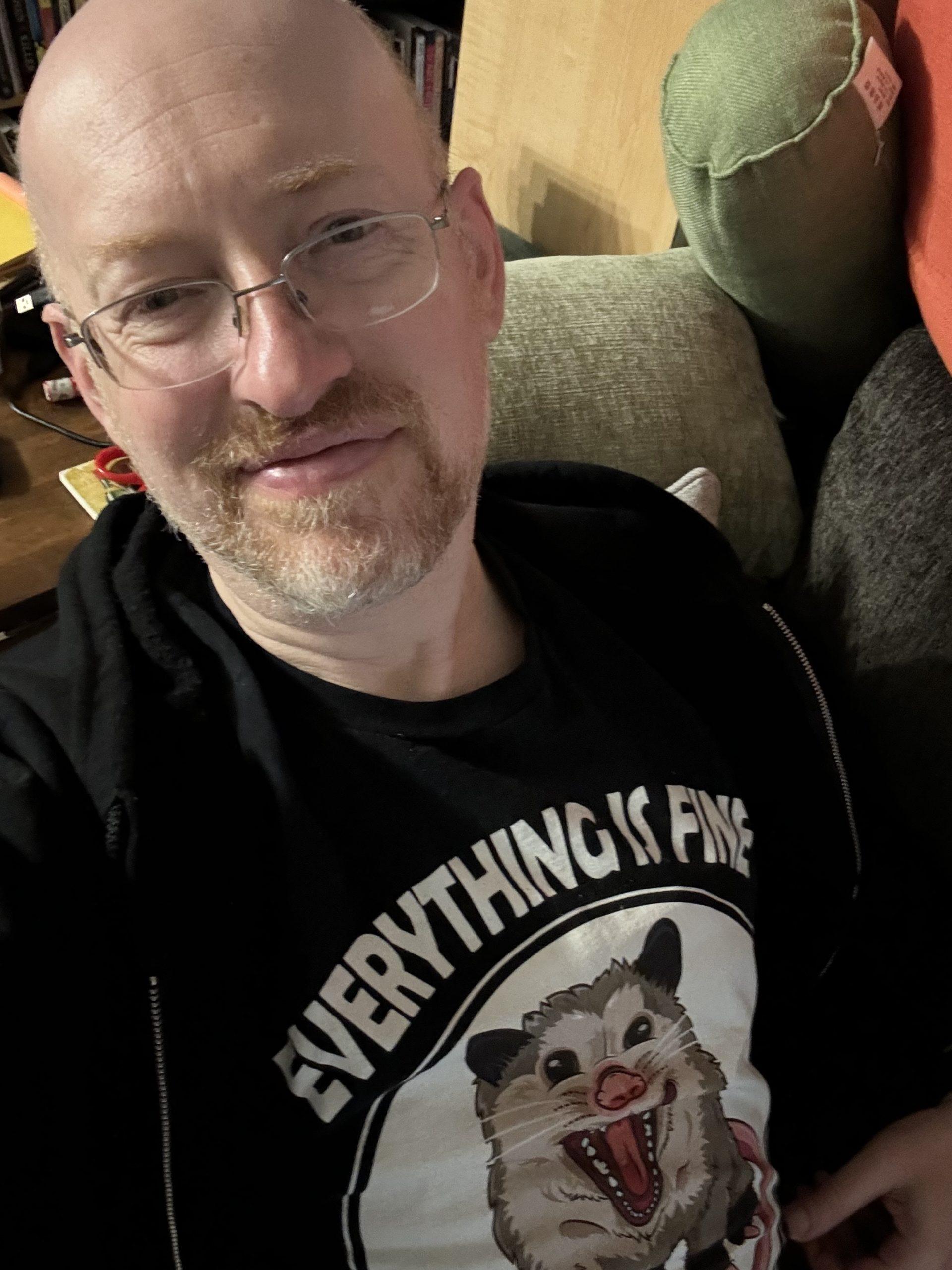 Me wearing a black t-shirt with an illustration of a hissing oppossum and the words 'everything is fine'.