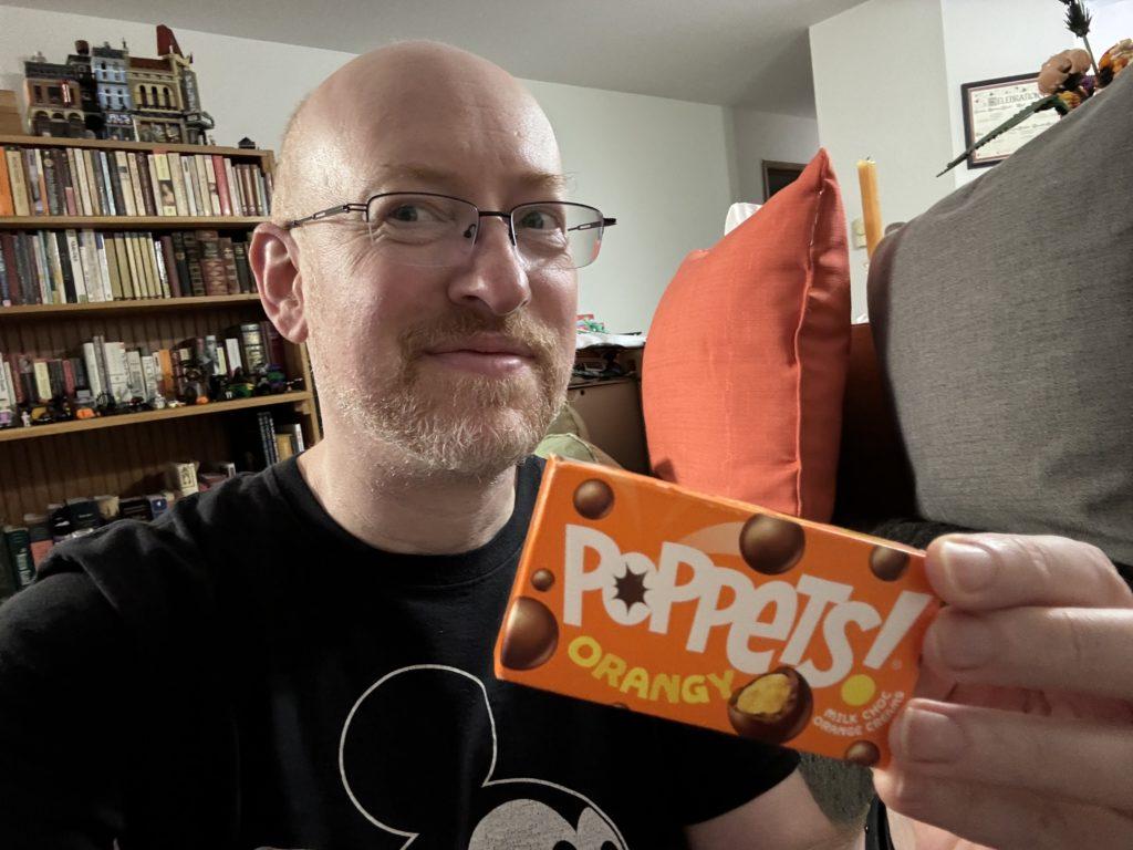 Me in my living room, holding a box of Poppets Orangy candy.