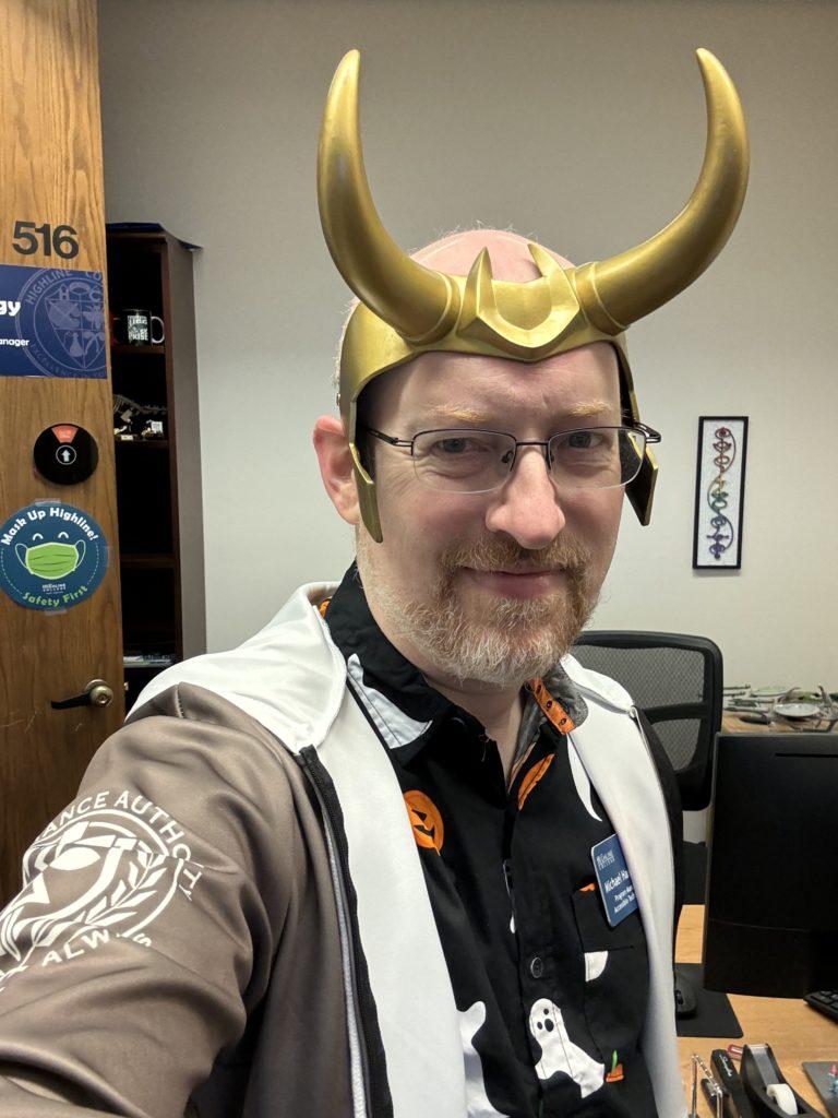 Me wearing a plastic Loki horned crown and a Time Variance Authority ‘Variant’ hoodie over a black button-up shirt with ghosts and Jack-o-Lanterns print.