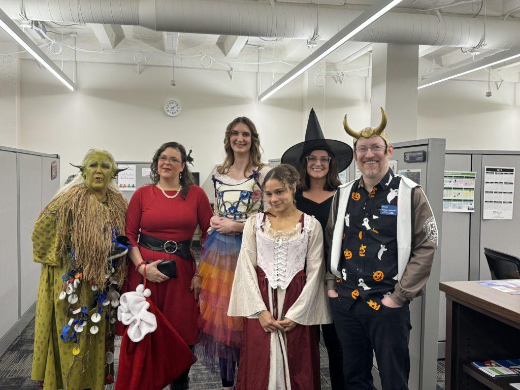 Me with five coworkers, all of us in Halloween costumes, including a sea hag, Santa, fairy, witch, and princess.