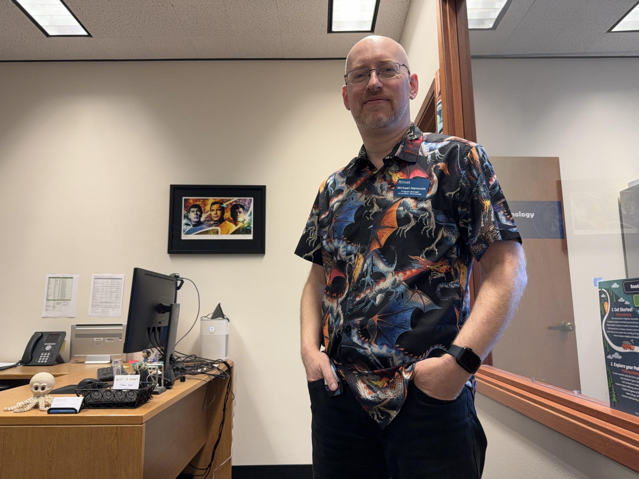 Me standing in my office, wearing a shirt with a print of dragons flying and breathing fire. Visible behind me is a Star Trek art print, and on my desk is a silly plastic octopus skeleton Halloween decor.