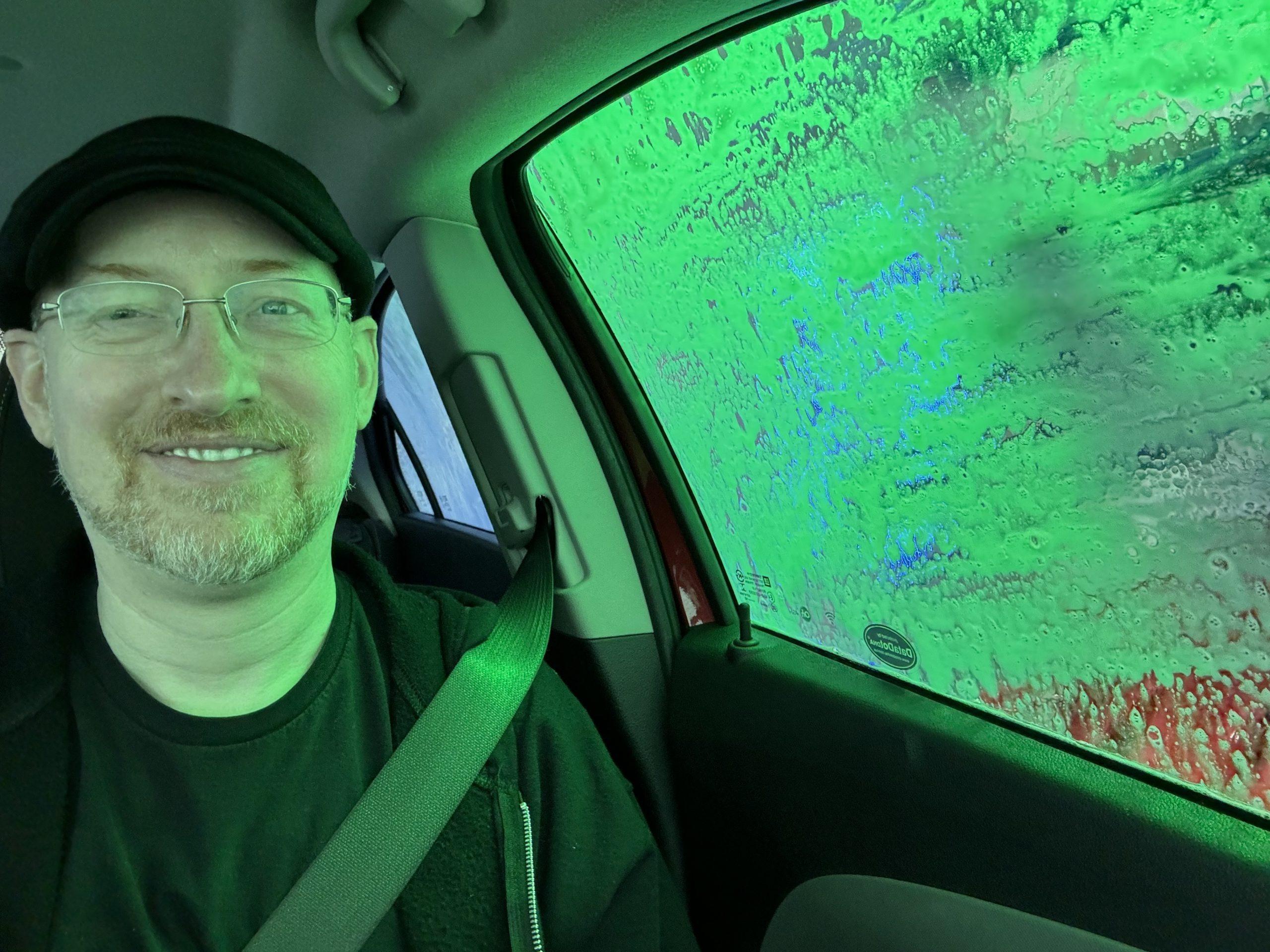 Me in the car, with soap covering the side window, and everything bathed in green light.