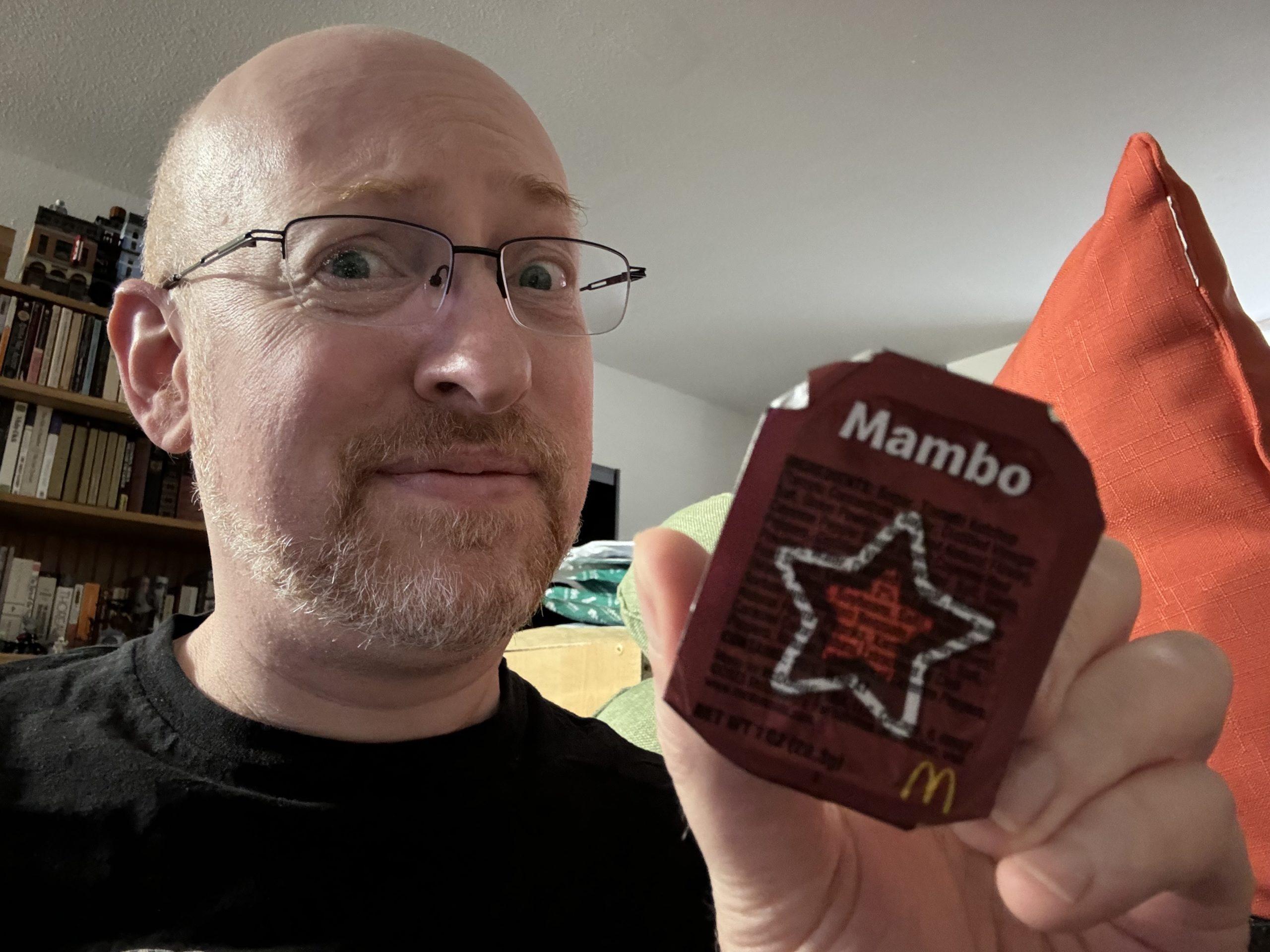 Me with a skeptical expression on my face, holding a McDonald's dipping sauce called 'Mango'.