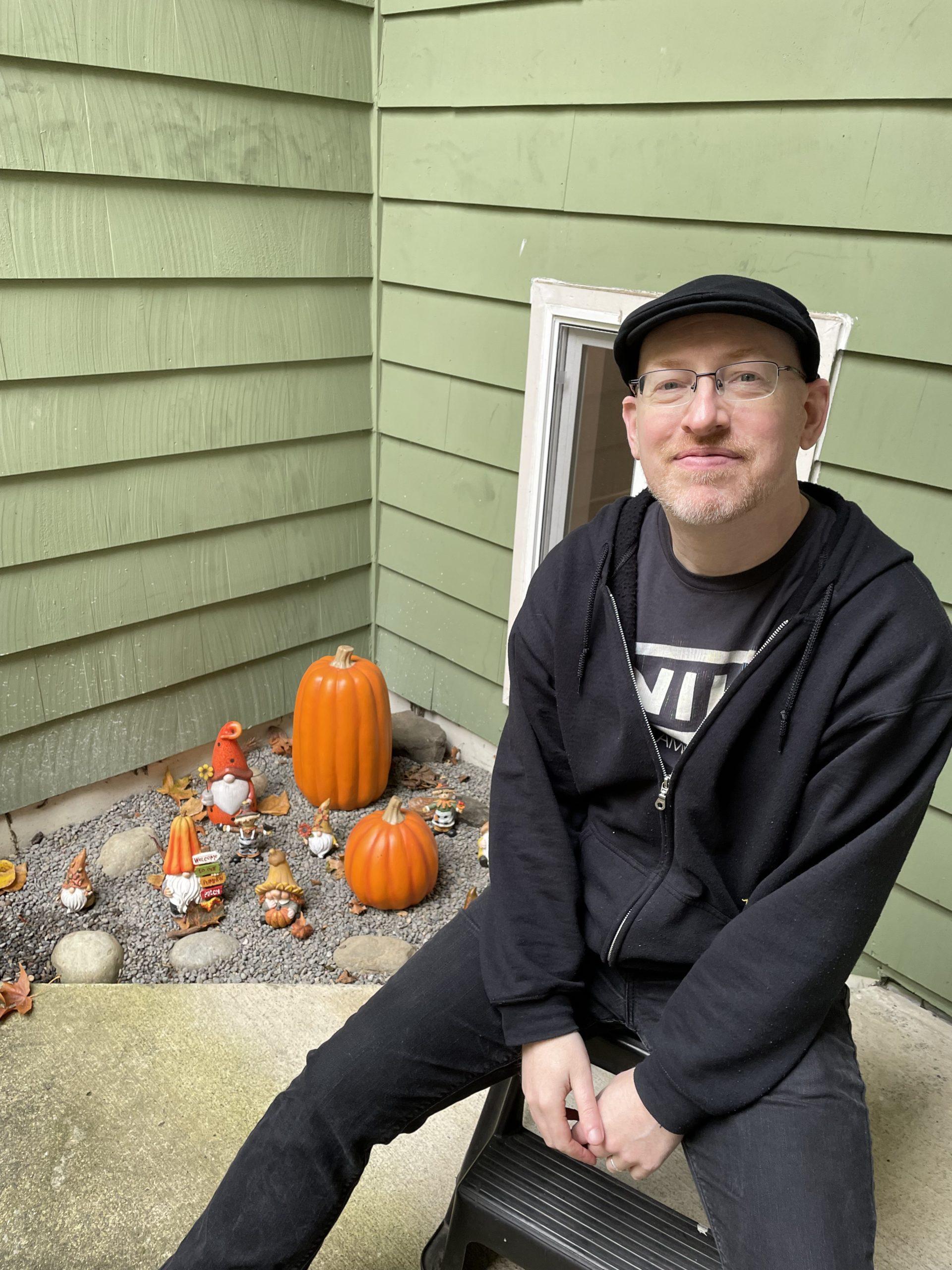 Me sitting on a footstep outside our home, in front of a collection of fall and Thanksgiving-themed decorative gnomes.