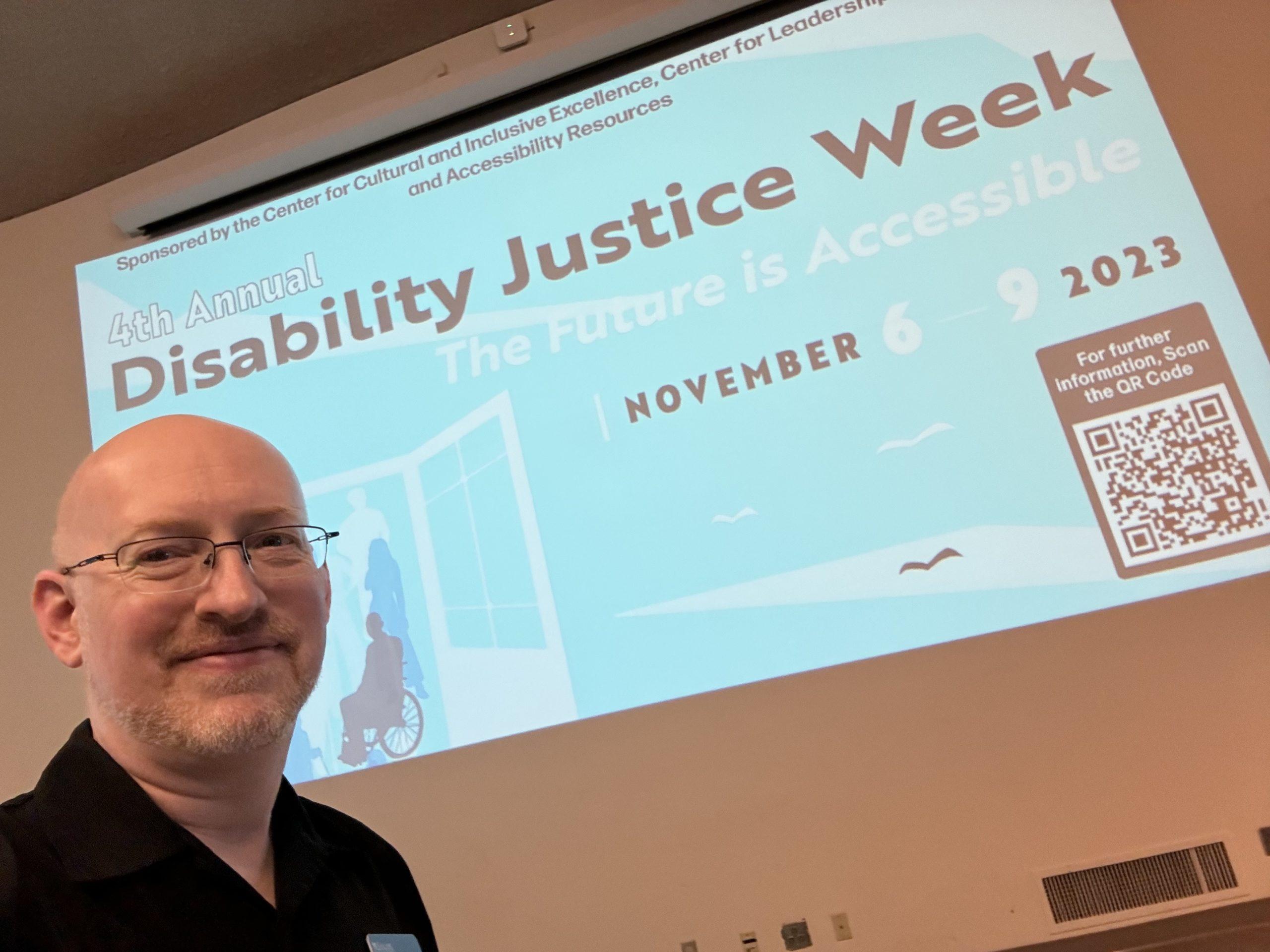 Me standing in front of a projected banner for Highline College's Disability Justice Week.