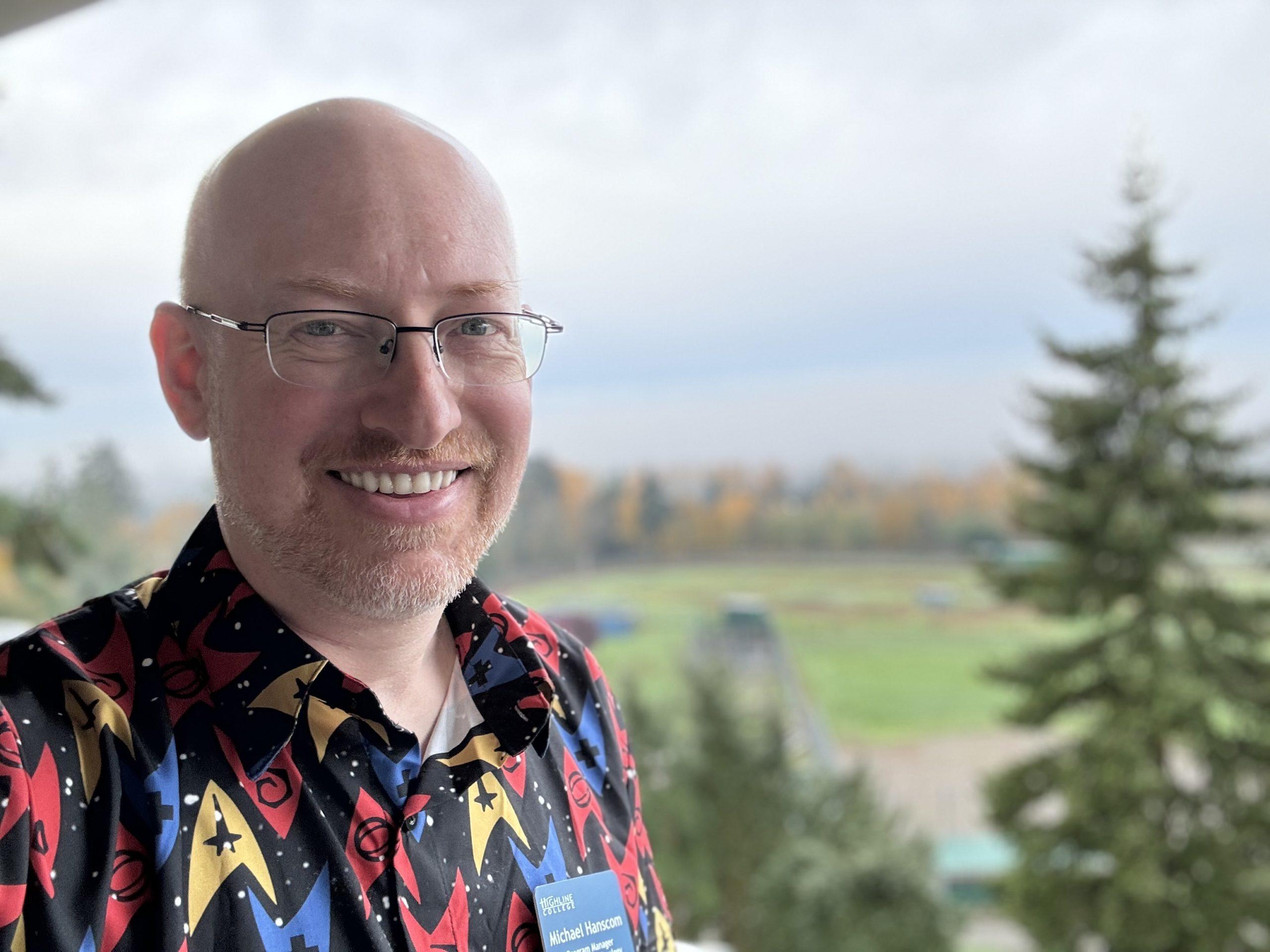 Me wearing a button-up shirt with Star Trek Starfleet division delta shield logos, in front of a blurred view of fall trees.