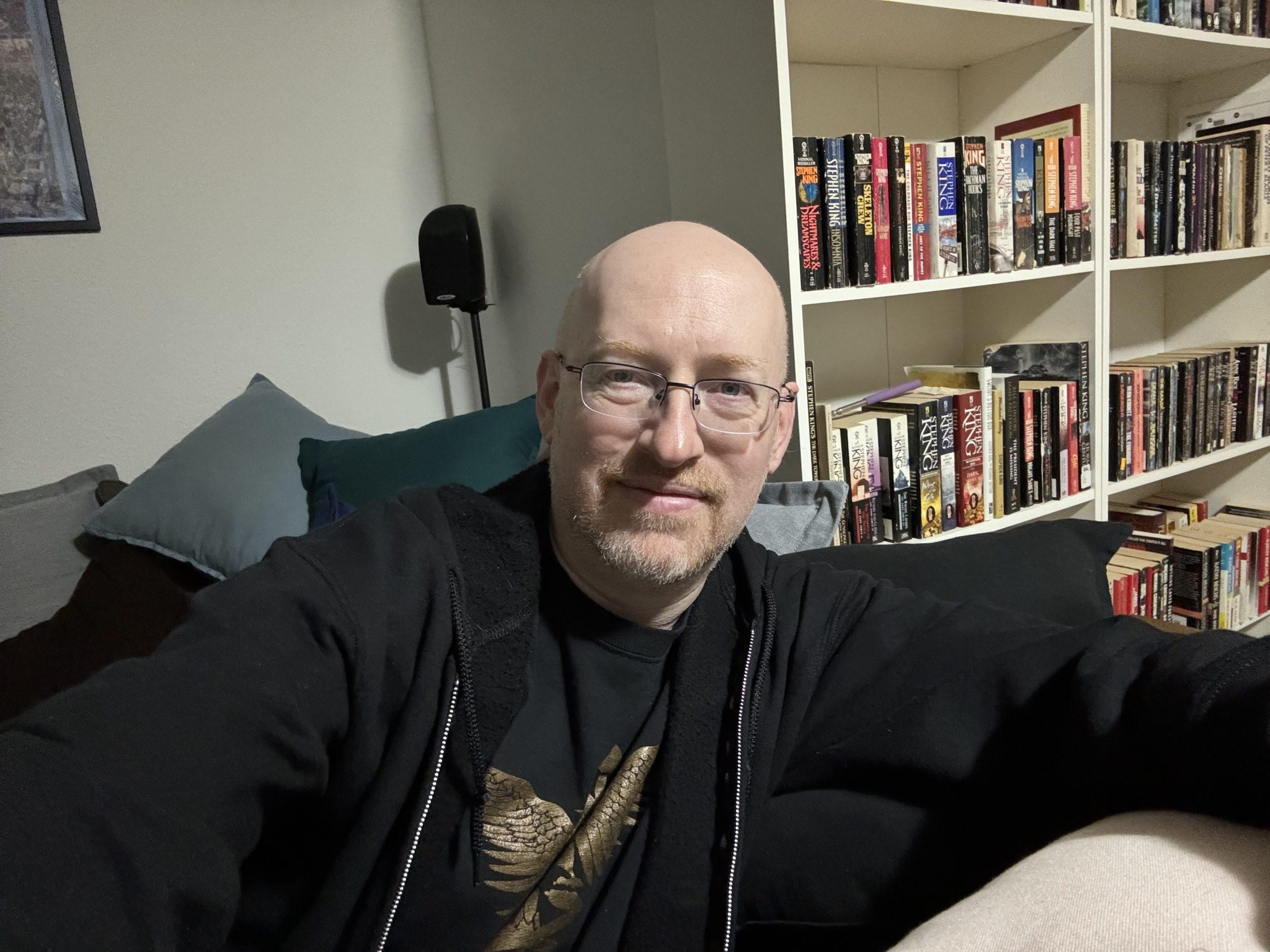 Me sitting in the corner of a couch, with a bookshelf full of Stephen King books visible behind me.