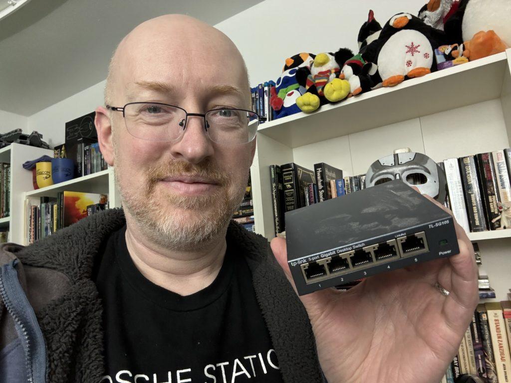 Me holding a dusty five-port Ethernet switch.