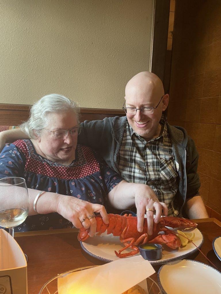 Me sitting next to my mom in a booth at a Red Lobster restaurant, as she arranges a lobster on a plate to be its most photogenic.