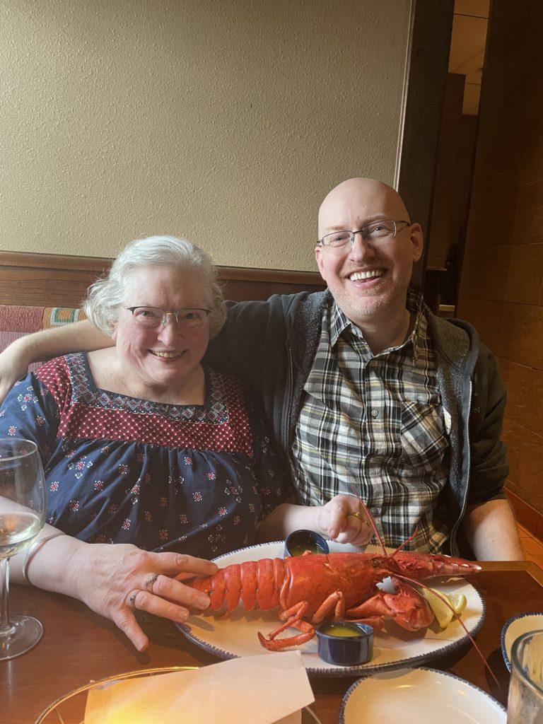 Me sitting next to my mom in a booth at a Red Lobster restaurant, with a huge lobster on a plate in front of her, about to be eaten.