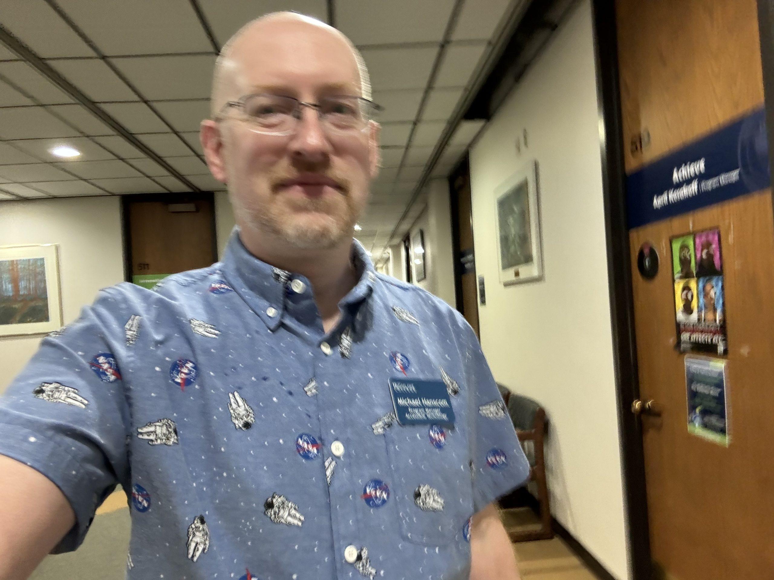 A slightly blurry shot of me walking down a college hallway, wearing a blue shirt with NASA logos and spacewalking astronauts.
