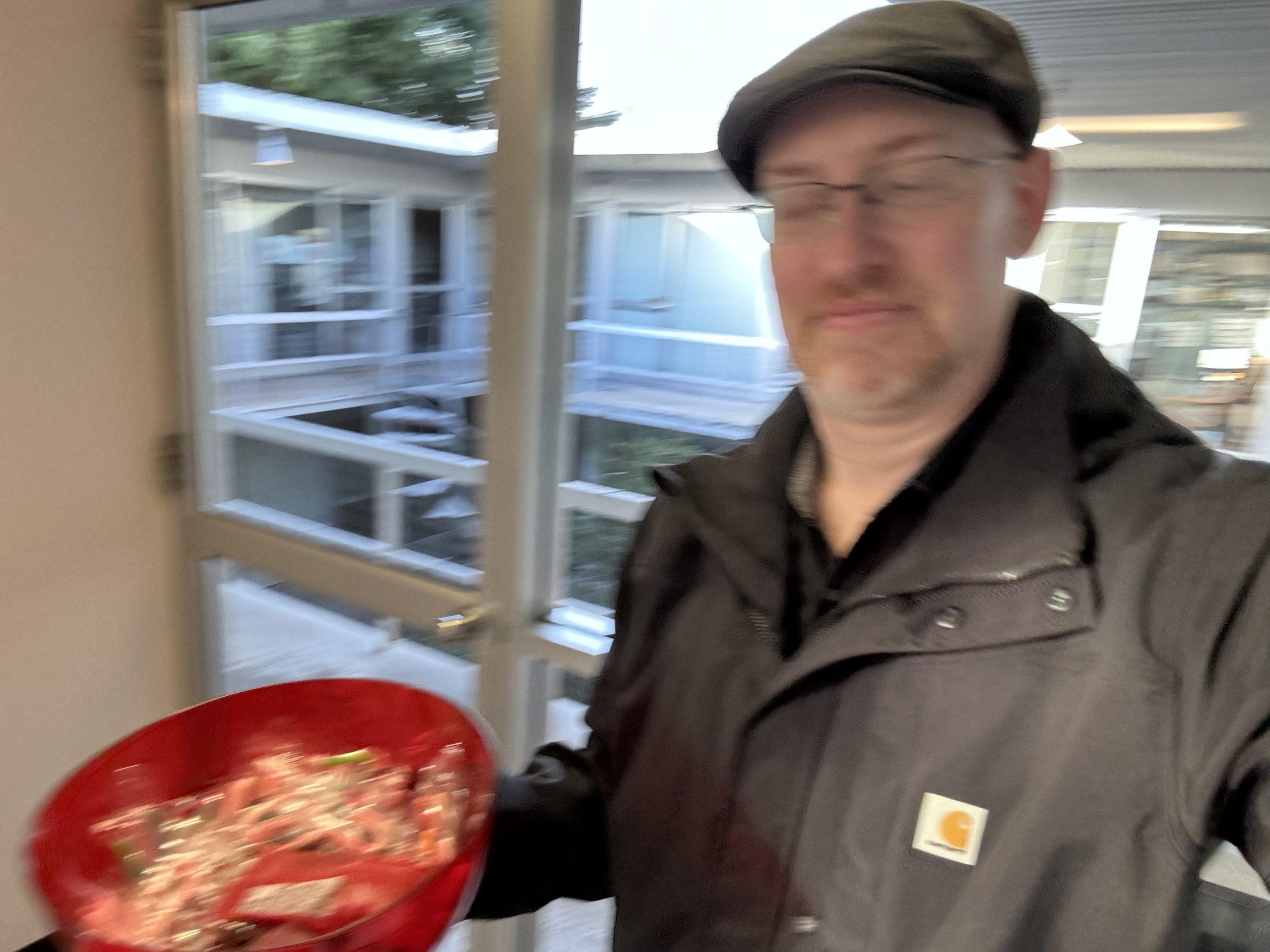 A blurry, badly shot selfie of me walking through a college building carrying a bnowl of holiday candy.