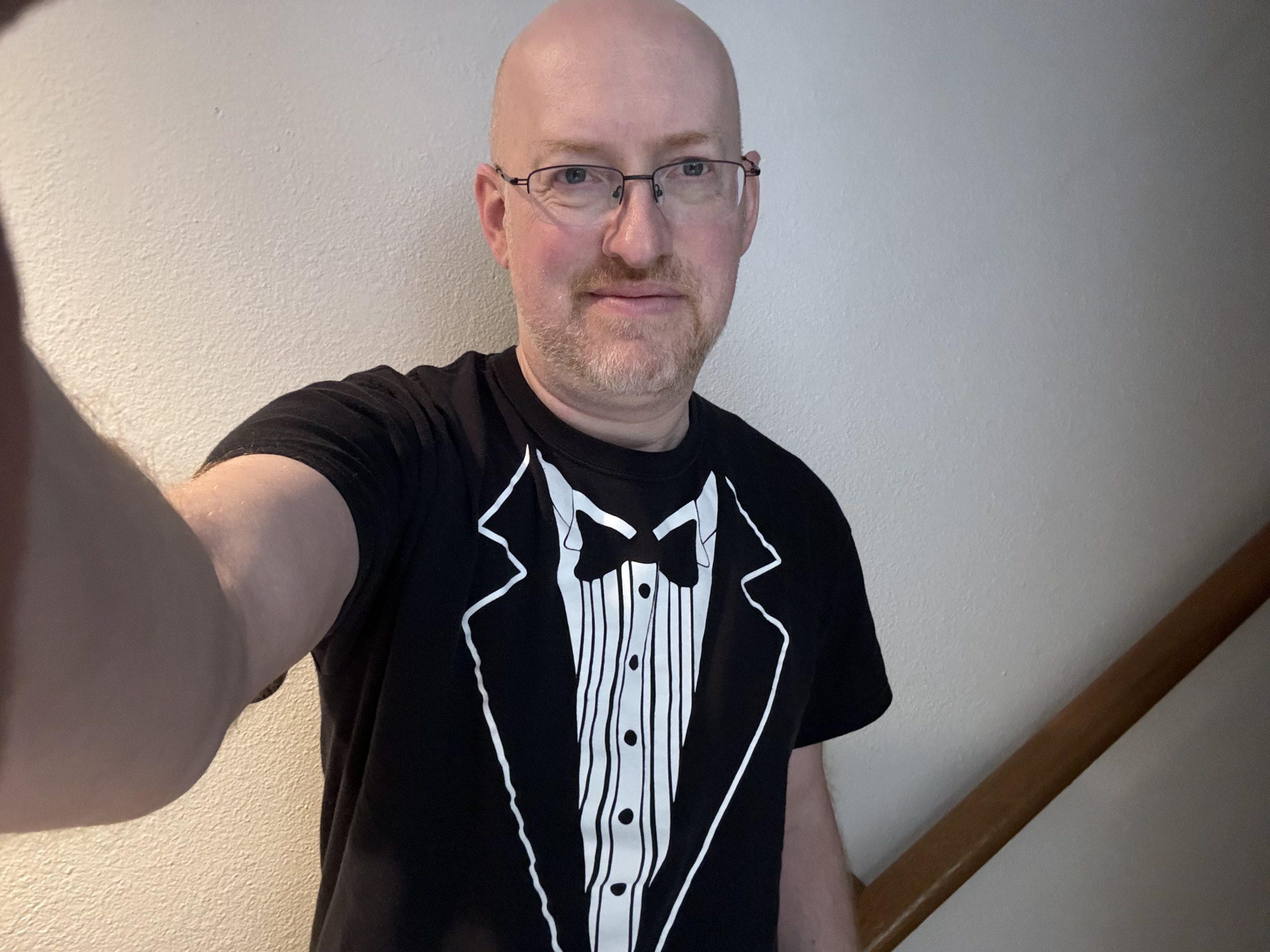 Me against a plain wall, wearing a novelty t-shirt printed to look like a tuxedo.