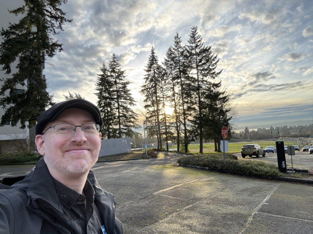 Me in the parking lot outside my work building, with the sun setting behind trees in the background.