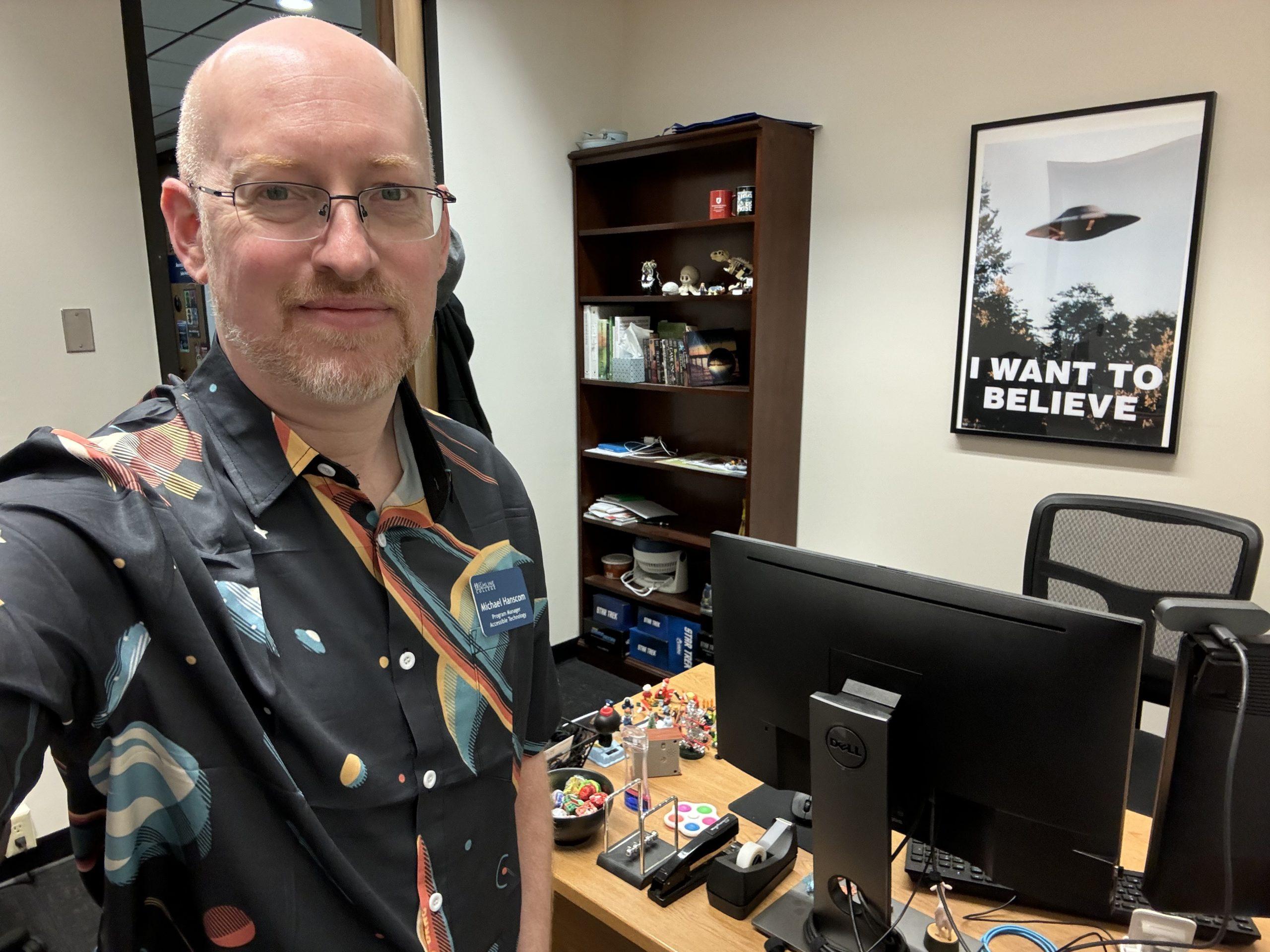 Me in my office at work, wearing a shirt with retro-styled planets and spaceships.