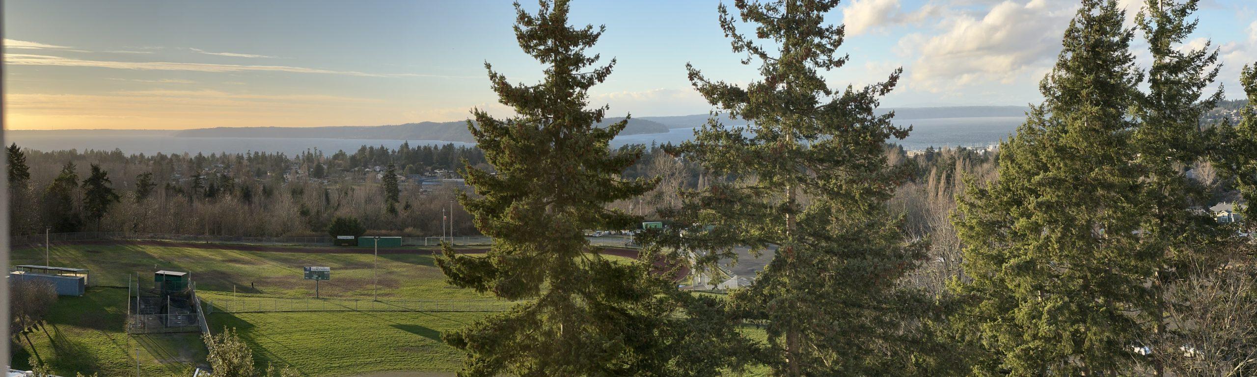 A panoramic shot of early sunset in a clear sky over green trees and the college sports fields.