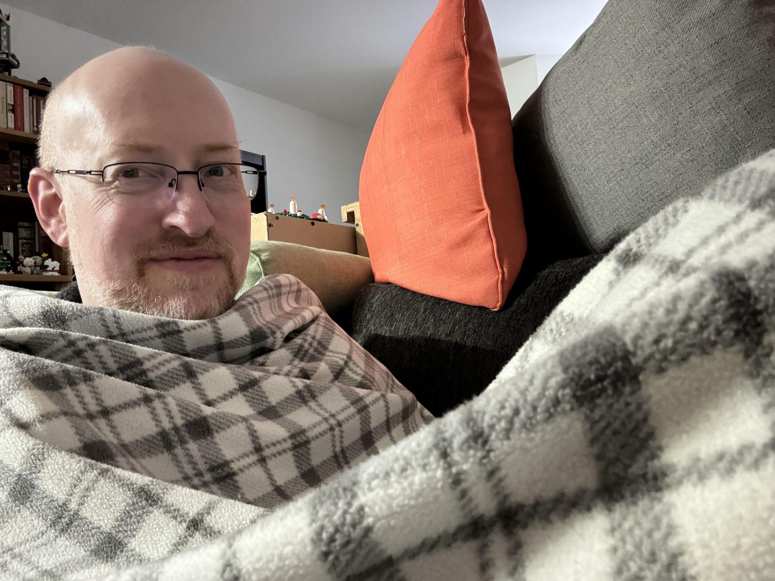 Me on our couch, wrapped up to my chin in a black-and-white plaid blanket.